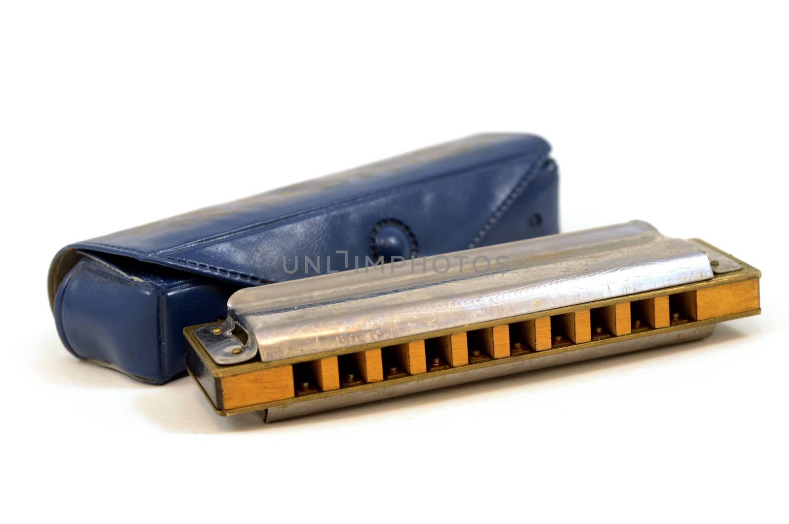 An isolated over a white background still-life image of a harmonica musical instrument and its original blue case.