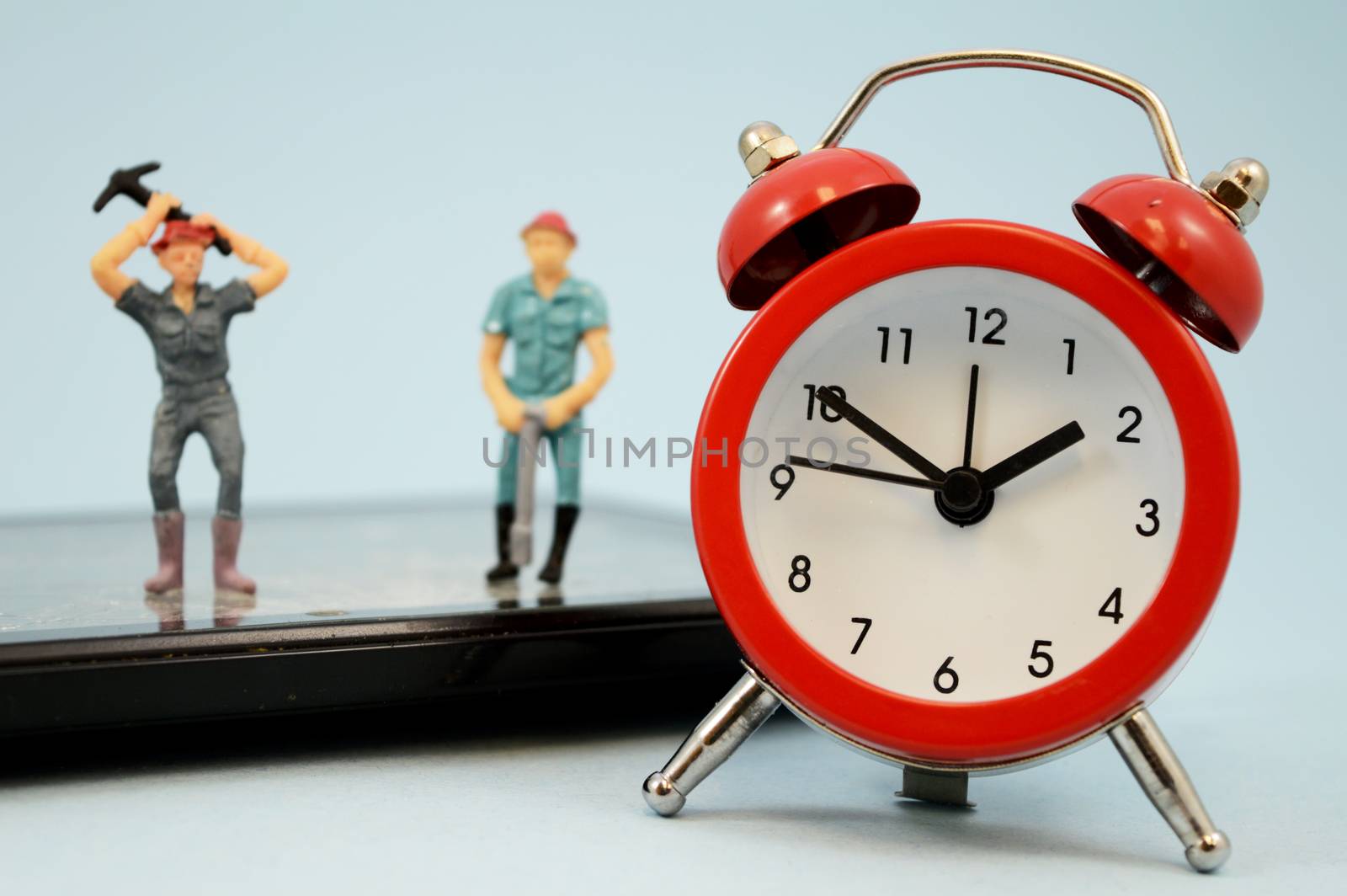 An illustrative concept showing some miniature labor workers or technical support hard at work on a damaged digital device with a red clock being the main plane of camera focus.