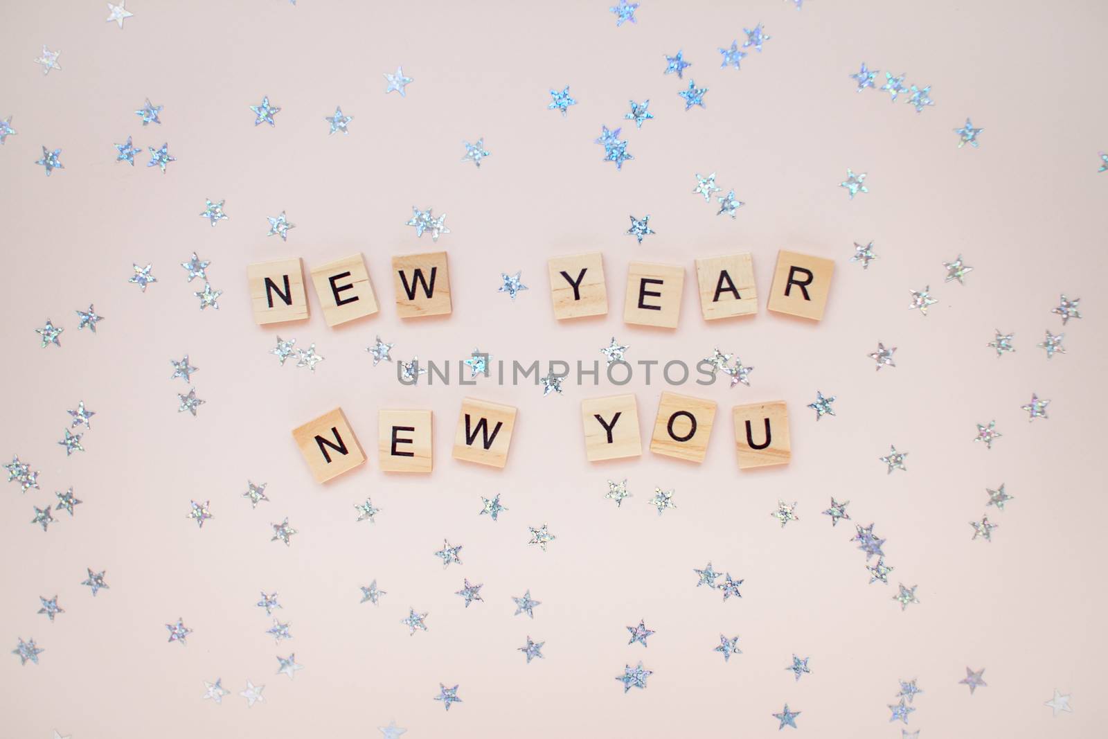 The inscription new year new you from wooden blocks on a light pink background. Silvery stars on a light pink background.