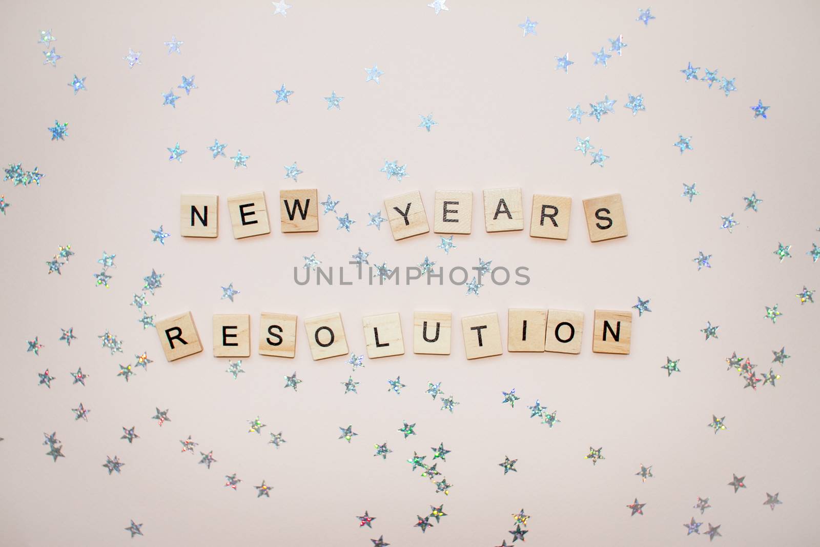 The inscription new years resolution from wooden blocks on a light pink background. Silvery stars on a light pink background.