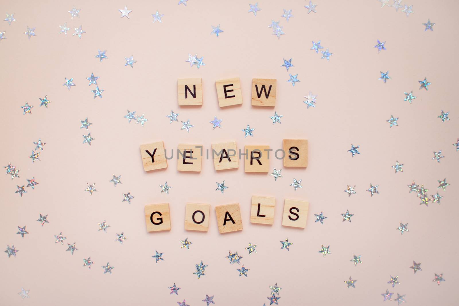 The inscription new years goals from wooden blocks on a light pink background. Silvery stars on a light pink background.