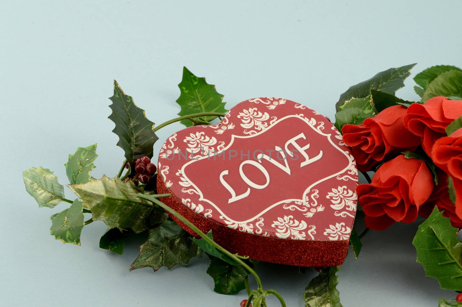 A romantic scene of a heart shaped box of chocolates with a bouquet of red roses.