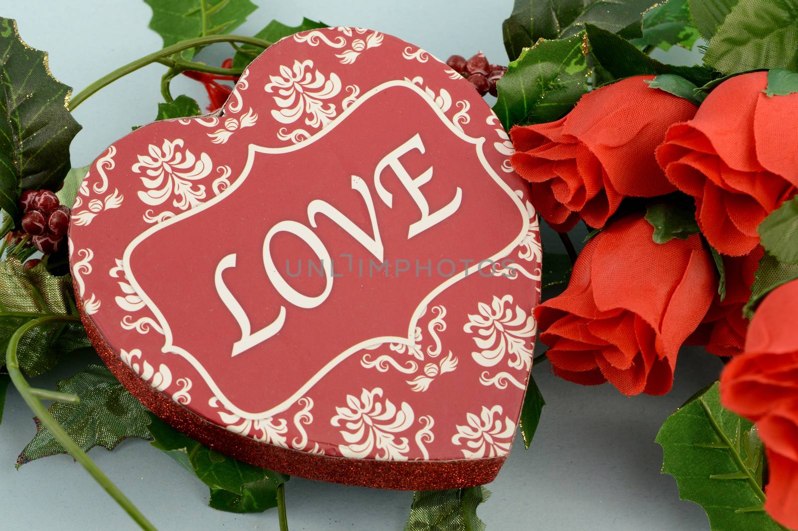 A romantic scene of a heart shaped box of chocolates with a bouquet of red roses.