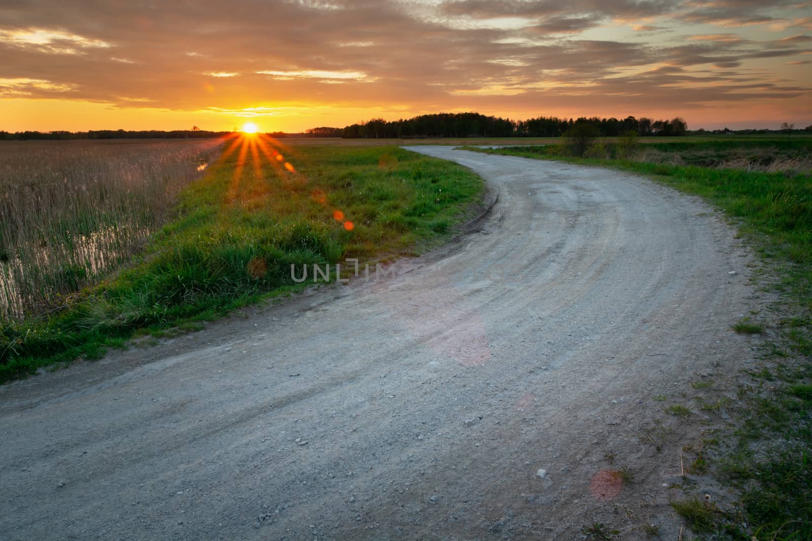 Ground road with stones and sunset, view in spring evening