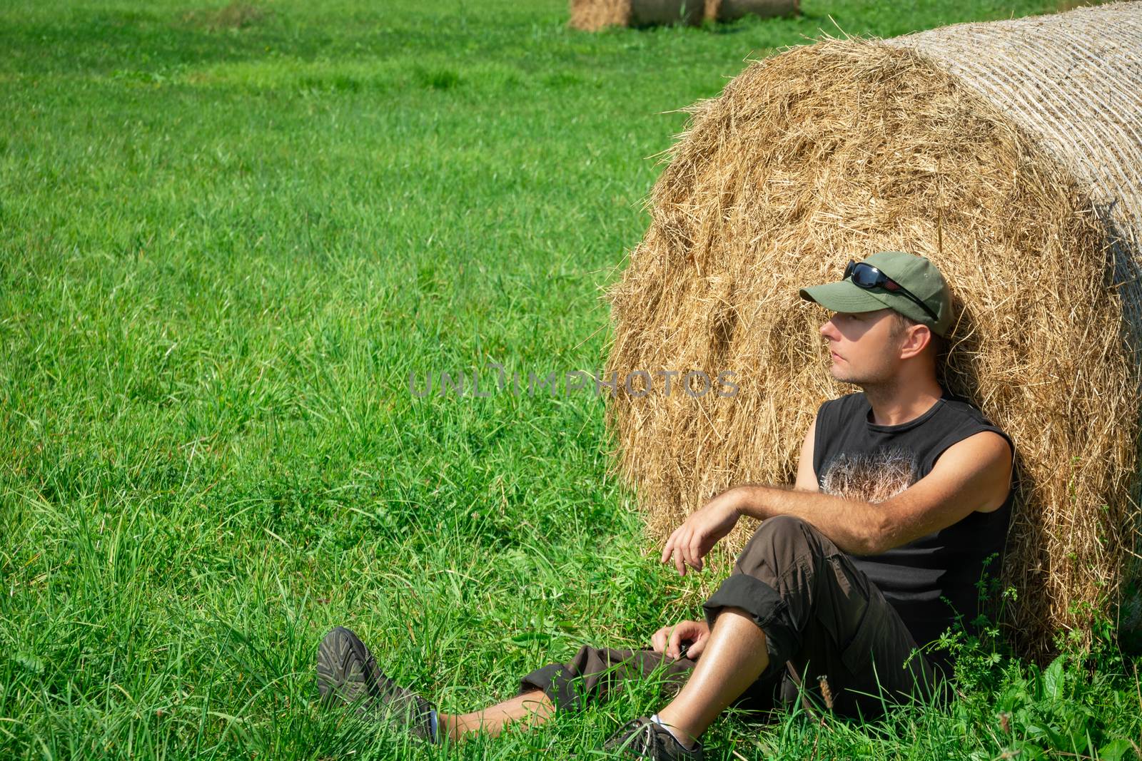 Sitting man to the green meadow, based on a hay bale, summer sunny day