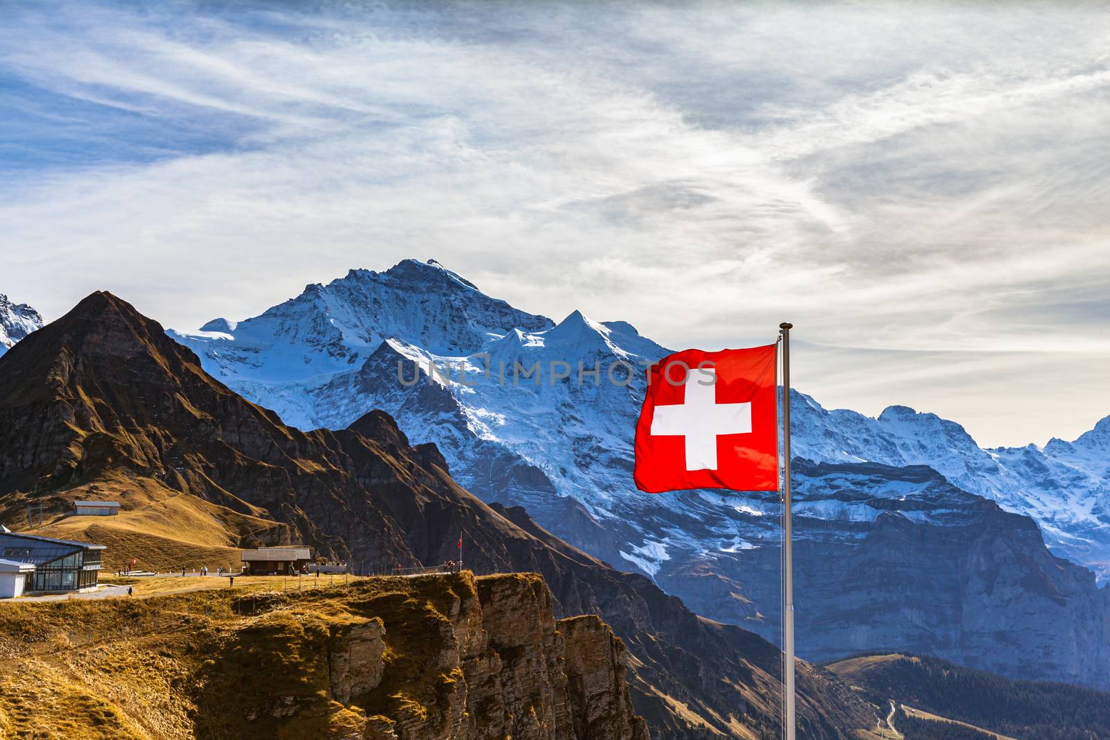 Stunning view of famous Jungfrau of Swiss Alps on Bernese Oberland from Mannlichen station, with Swiss national flag in foreground, on a sunny autumn day, Canton of Bern, Switzerland