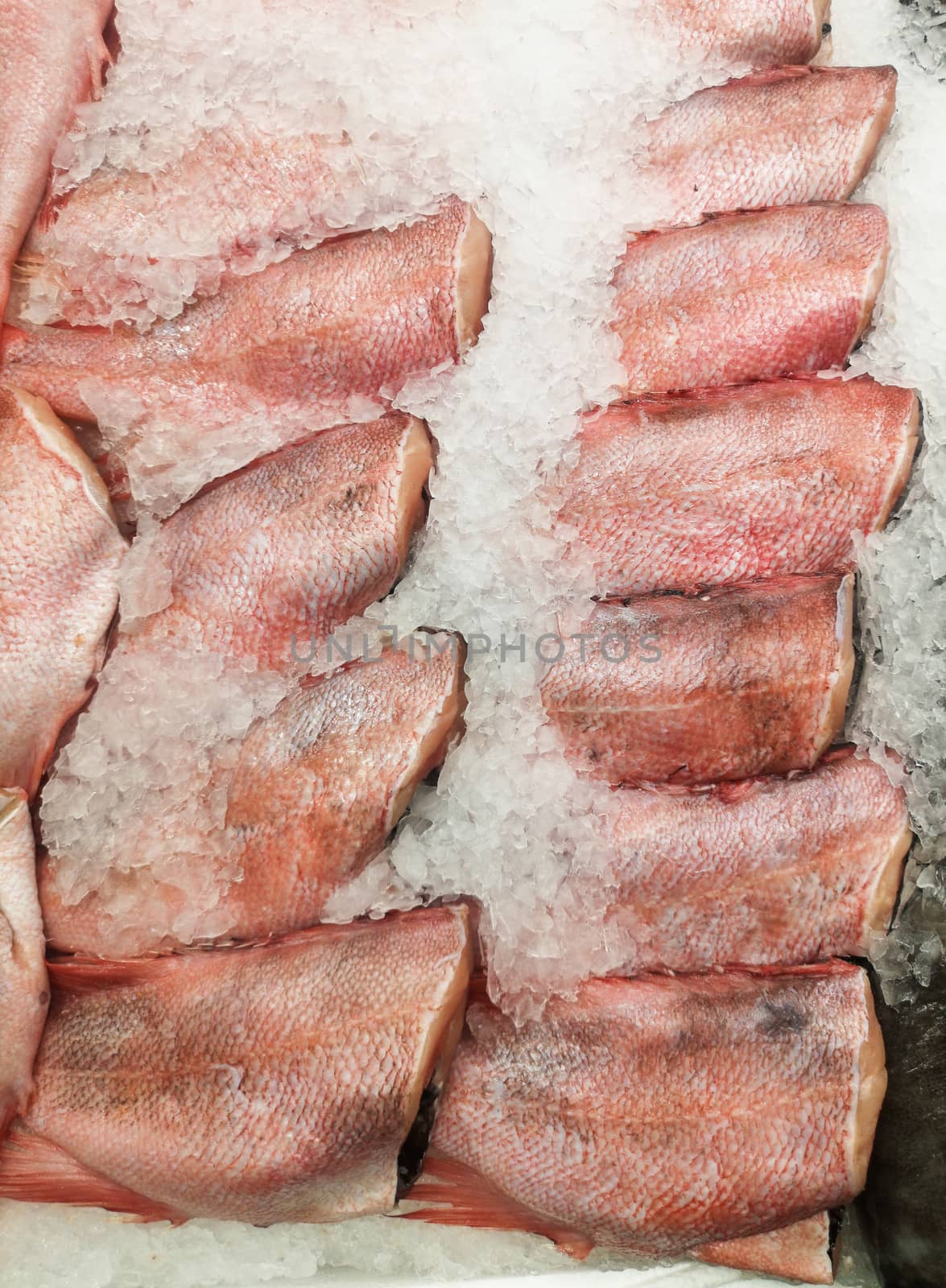 A chilled peeled headless fish carcass lying on ice in a shop window, store counter or supermarket.