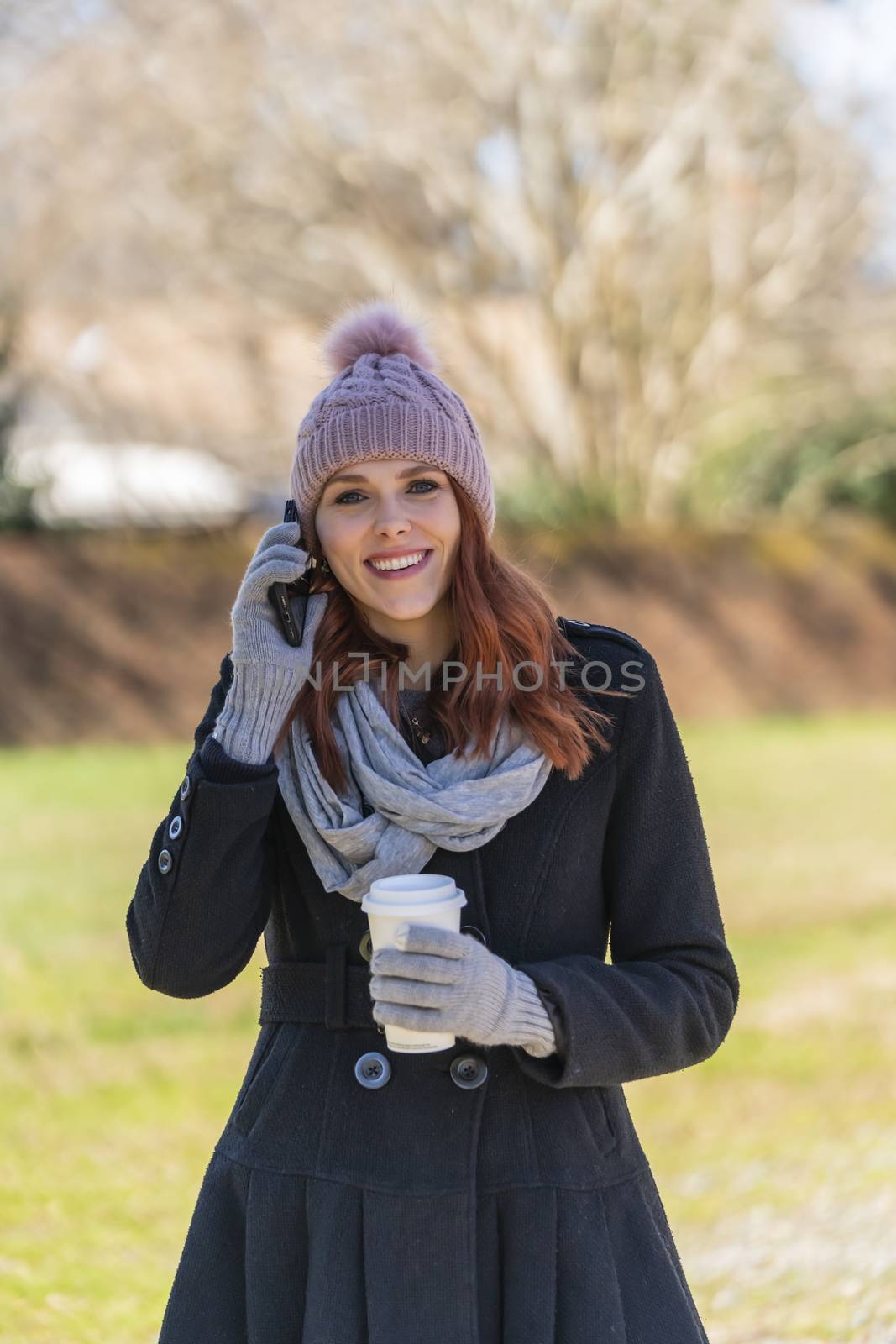 A gorgeous blonde model enjoys a winters day outdoors while drinking her favorite drink and talking on her cellphone