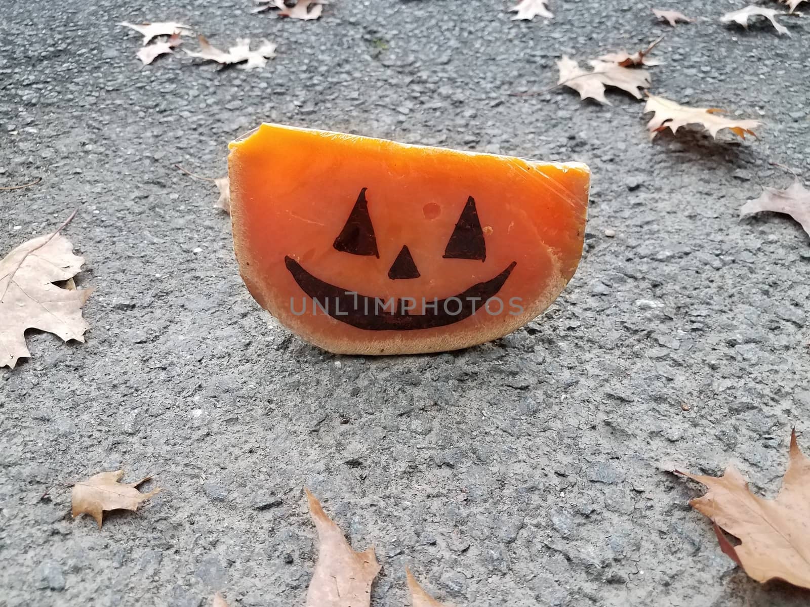 orange cheese with Halloween pumpkin face and asphalt and leaves