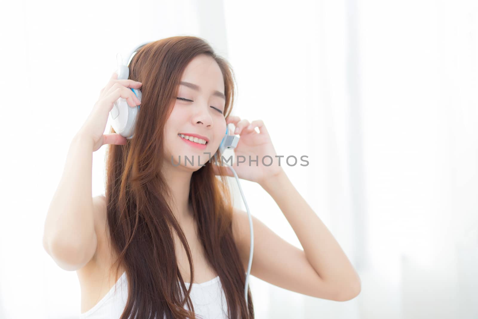 Beautiful asian young woman enjoy listen music with headphone while sitting in bedroom, relax girl with earphone internet online, leisure and technology concept.