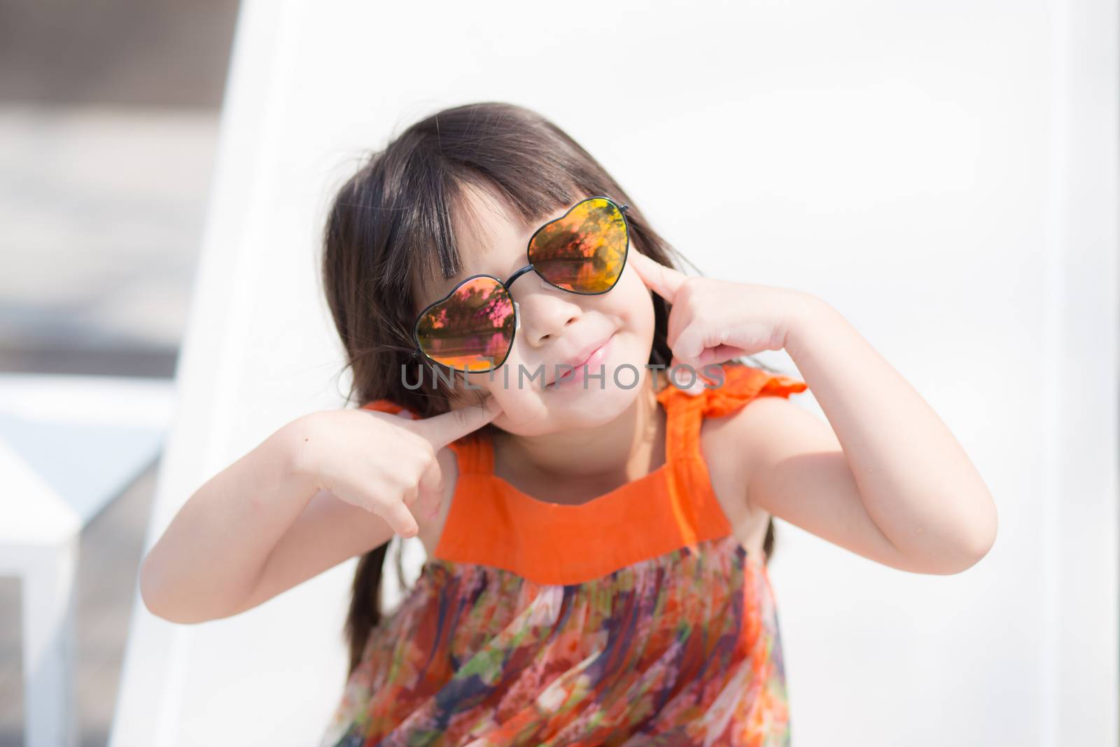 Beautiful portrait little girl asian of a smiling sitting at swimming pool, kid leisure and joyful wear glasses in outdoor.