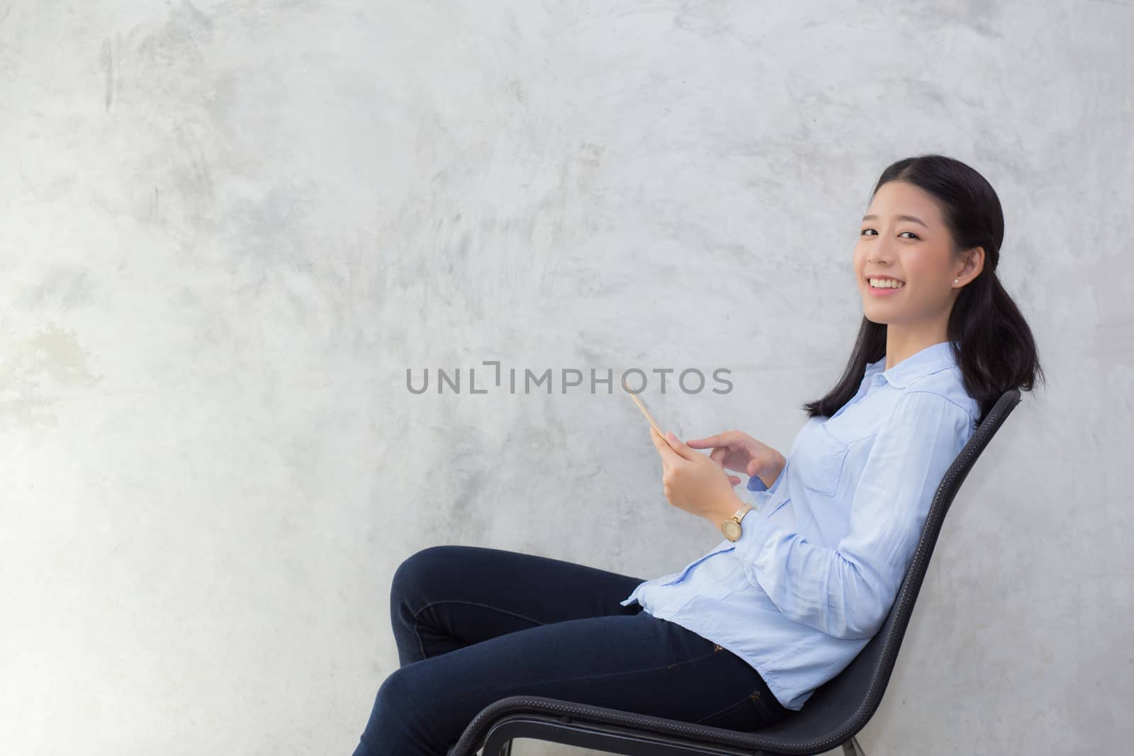 Beautiful young asian woman touching tablet computer and smile sitting on cement background, freelancer female calling telephone, communication concept.