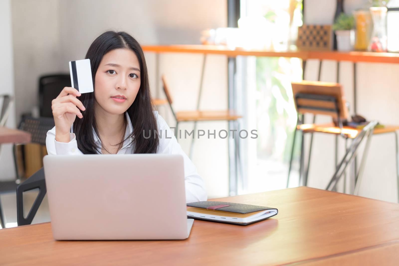 Beautiful young asian woman holding a credit card and shopping online with using laptop computer at cafe, girl payment on notebook to internet, business ecommerce and lifestyle concept.