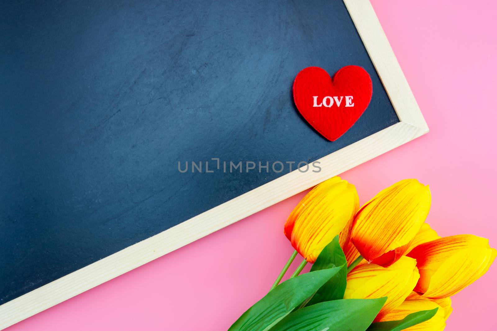 Beautiful of yellow tulip flower and chalkboard, blackboard and pillow heart shape with flat lay on the pink background, top view, copy space, mother day and holiday concept.
