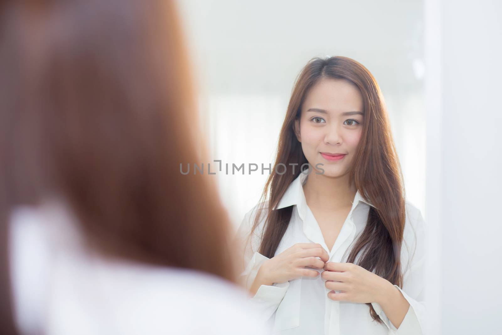Beautiful of portrait asian young woman examining with face and smile looking on mirror at bedroom, girl beauty of makeup and dressed up with reflection, lifestyle and wellness concept.