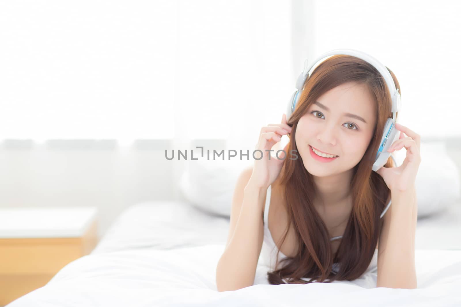 Beautiful asian young woman enjoy listen music with headphone while lying in bedroom, relax girl with earphone internet online, leisure and technology concept.