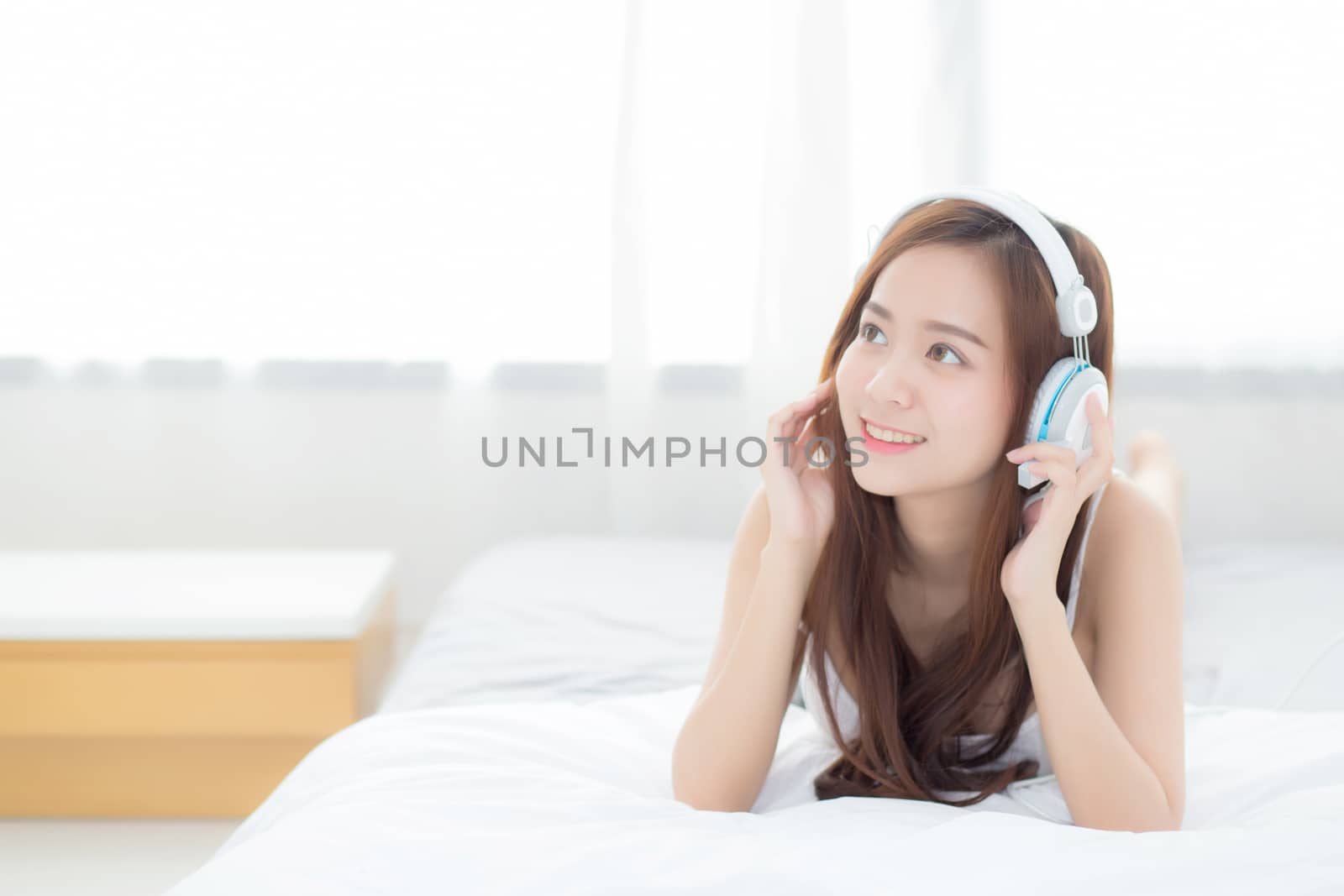 Beautiful asian young woman enjoy listen music with headphone while lying in bedroom, relax girl with earphone internet online, leisure and technology concept.