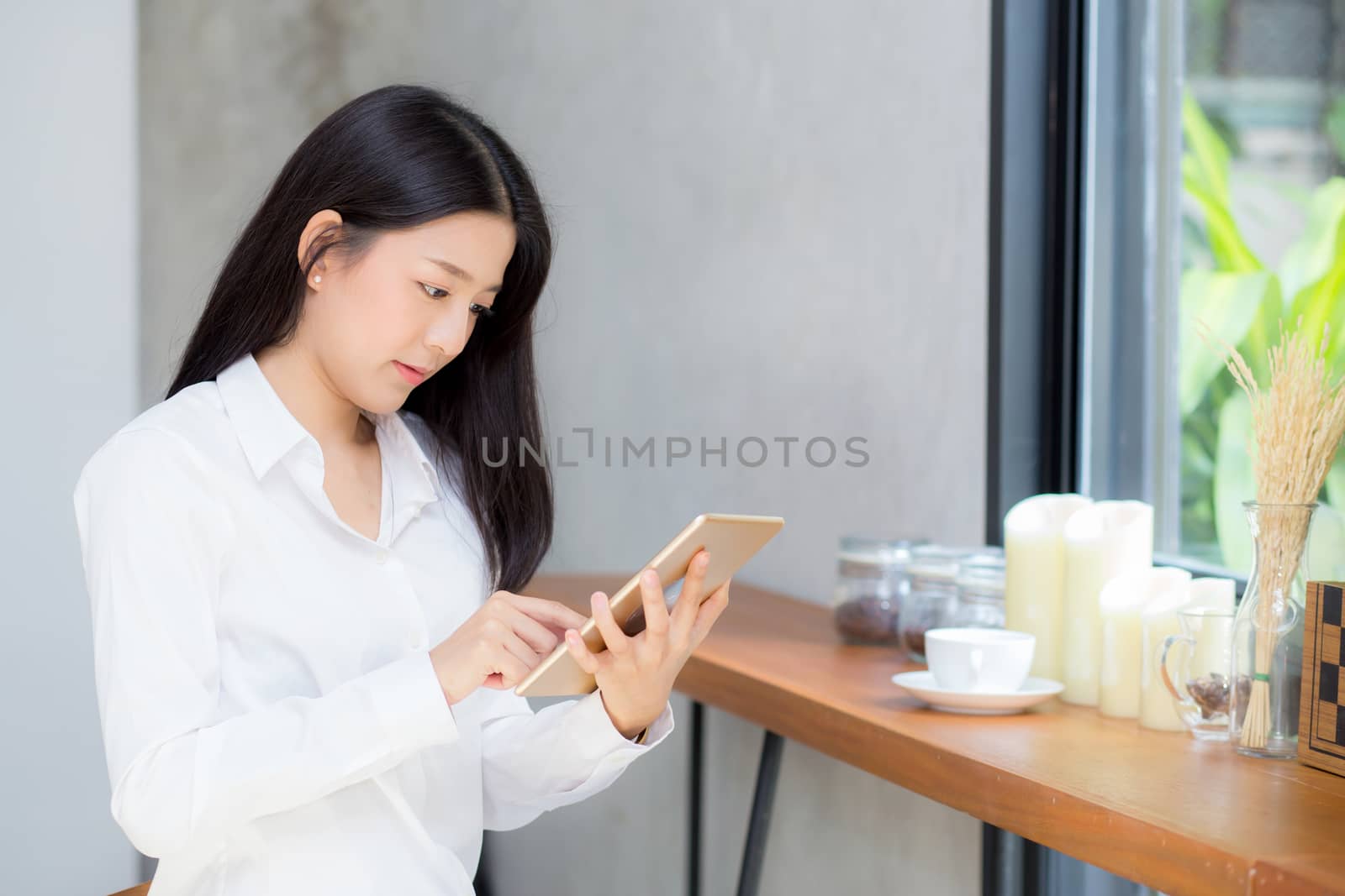 Beautiful portrait young asian woman using tablet computer in the coffee shop, businesswoman sitting looking tablet is work at cafe, communication concept.