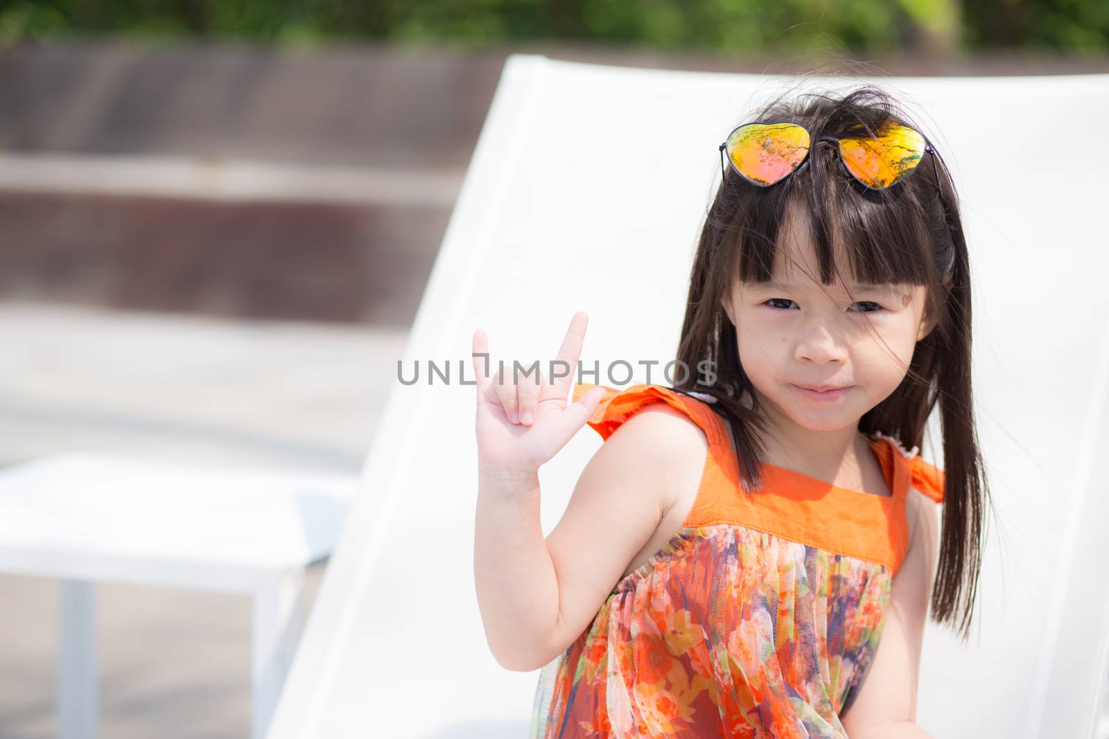 Beautiful portrait little girl asian of a smiling sitting at swimming pool, kid leisure and joyful wear glasses in outdoor.
