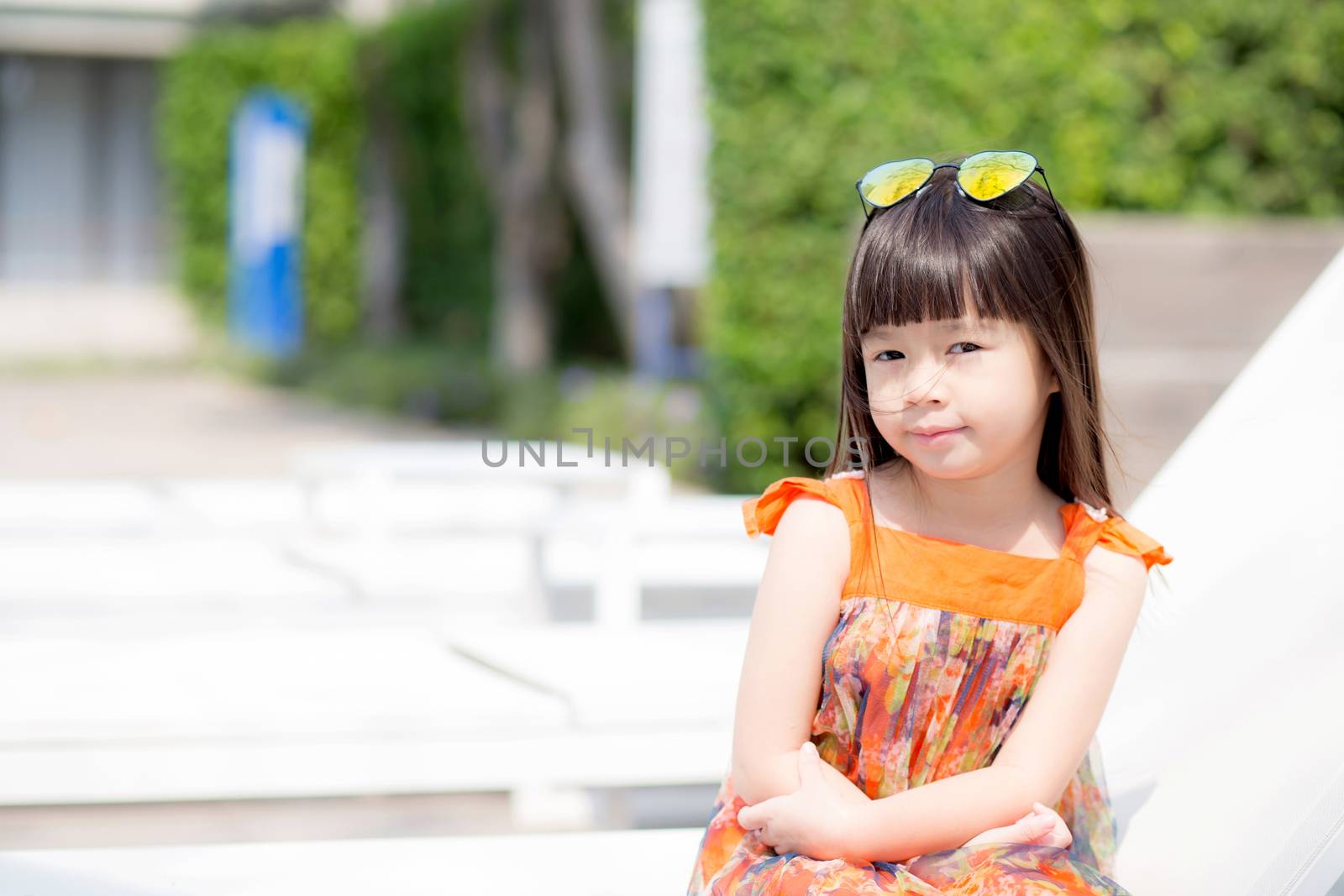 Beautiful portrait little girl asian of a smiling sitting at swimming pool, kid leisure and joyful wear glasses in outdoor.