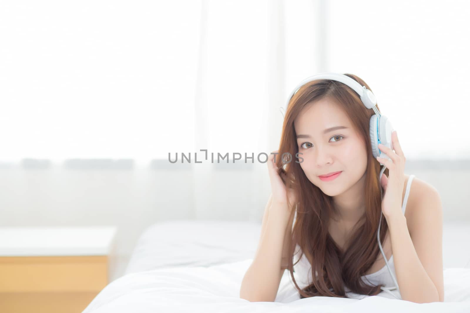 Beautiful asian young woman enjoy listen music with headphone while lying in bedroom, relax girl with earphone internet online, leisure and technology concept.