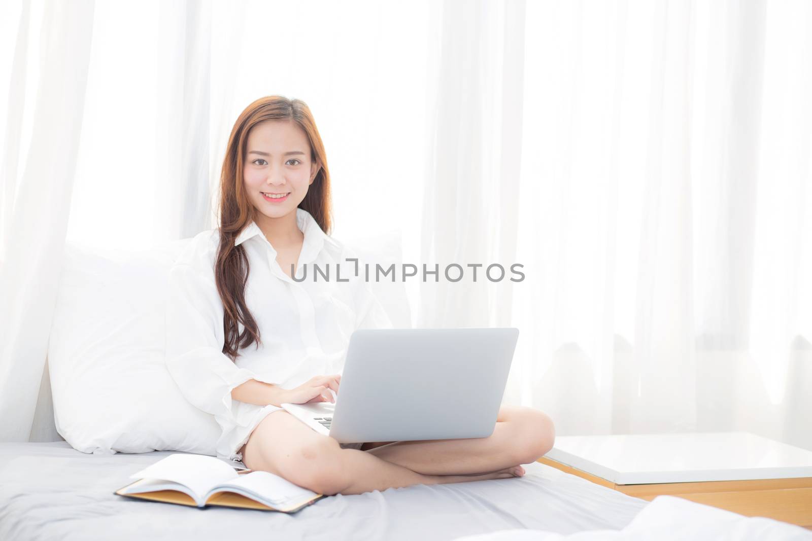 Beautiful of portrait asian young woman setting on bed using laptop computer and notebook at bedroom for leisure and relax, freelance with girl working at bedroom with note, communication and lifestyle concept.