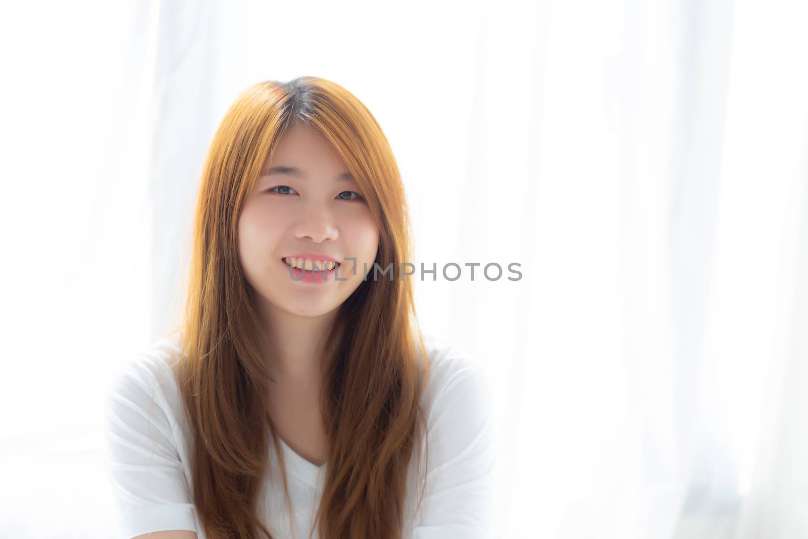Portrait of beautiful young asian woman standing the window and smile while wake up with sunrise at morning, lifestyle and relax concept.