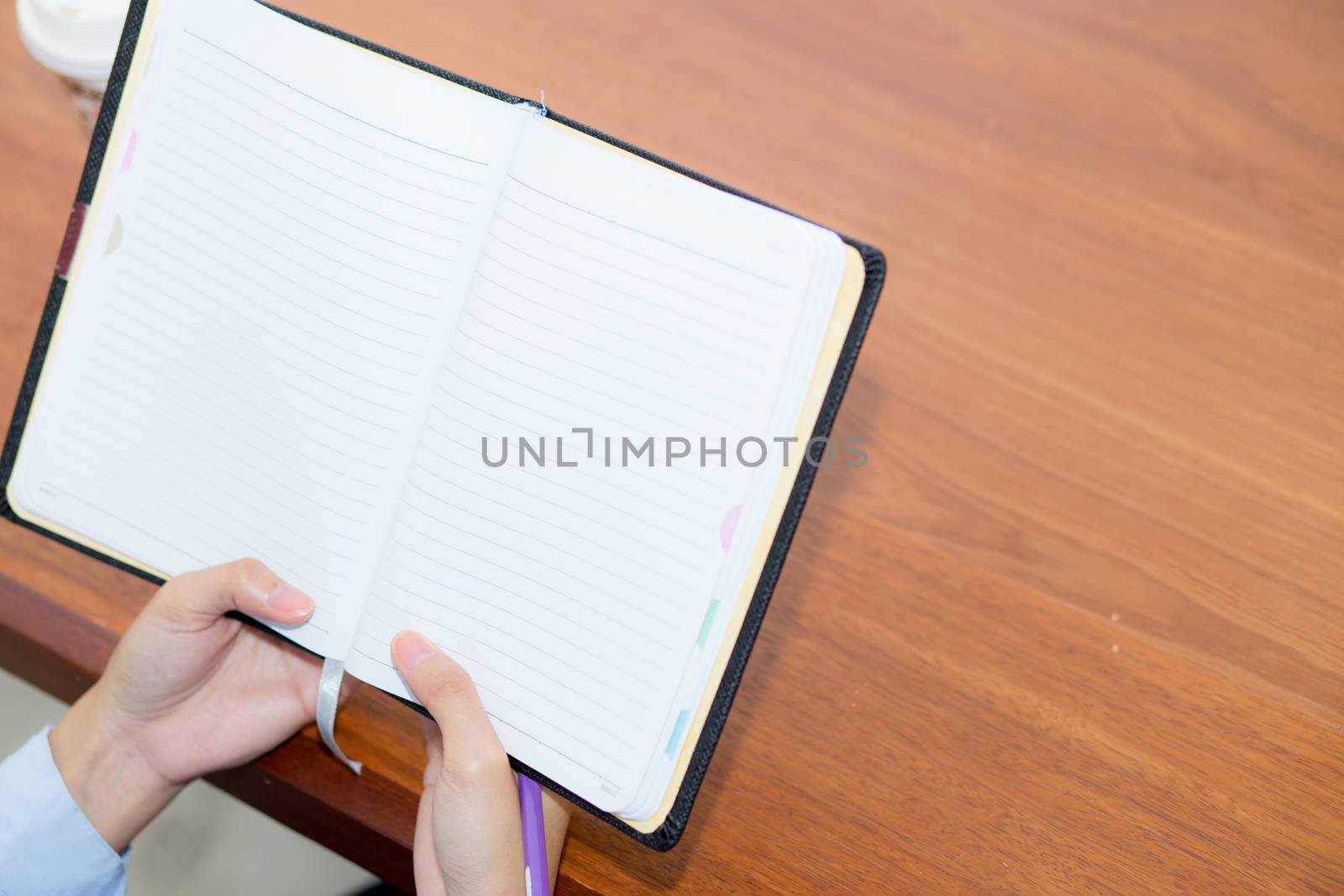 closeup woman hand writing on notebook on wooden table, girl work with paper at coffee shop, top view; freelance business concept.
