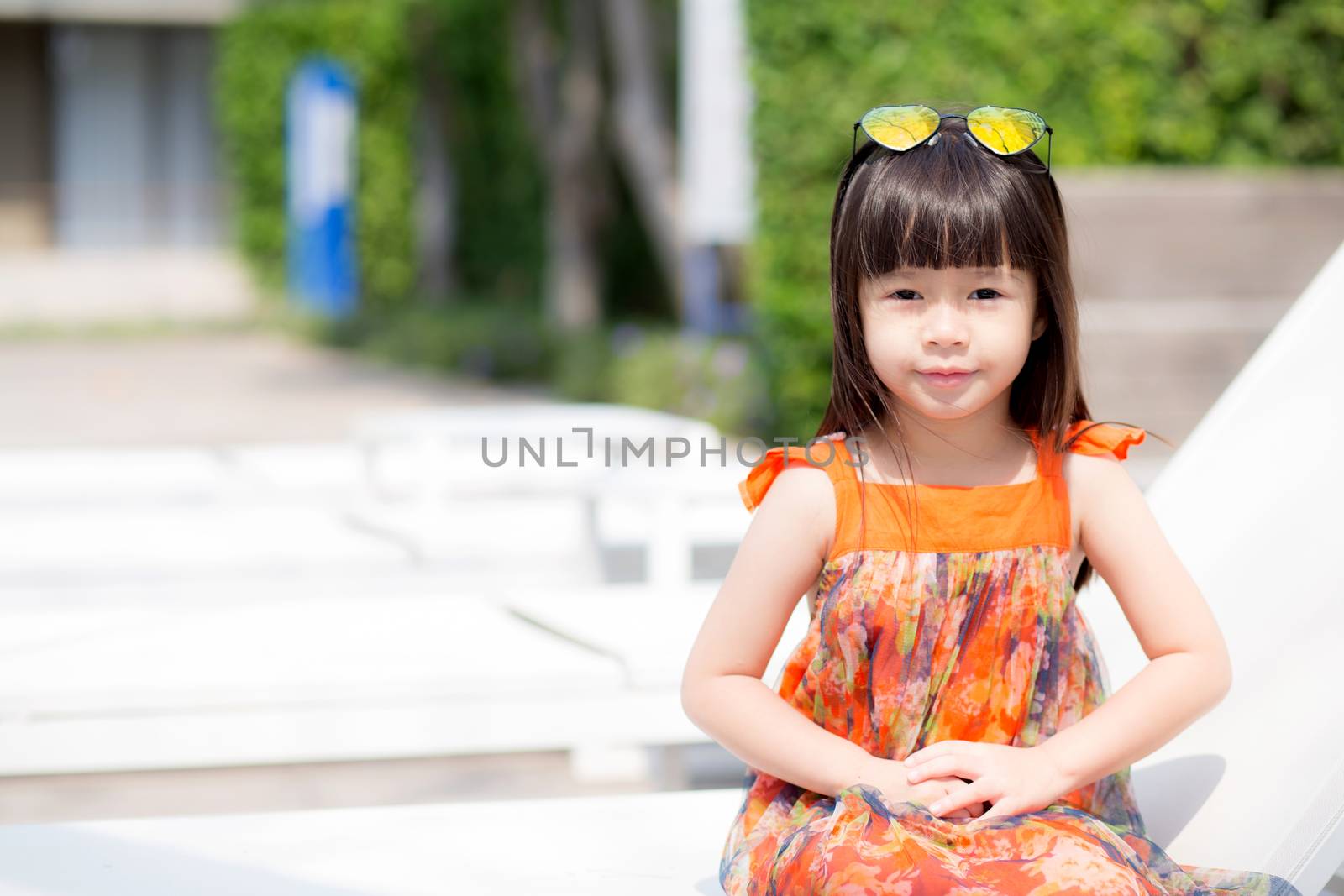 Beautiful portrait little girl asian of a smiling sitting at swimming pool, kid leisure and joyful wear glasses in outdoor.