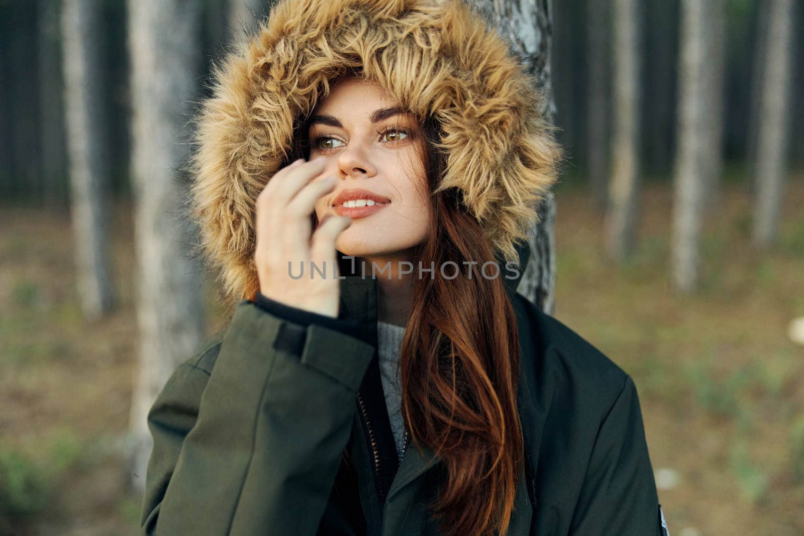 woman in autumn forest on warm jacket with a hood holds her hand near her face by SHOTPRIME