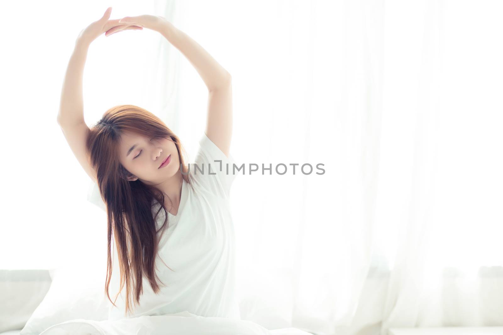 Beautiful young asian woman stretch and relax in bed after wake up morning at bedroom, back view, new day and resting for wellness, lifestyle concept.
