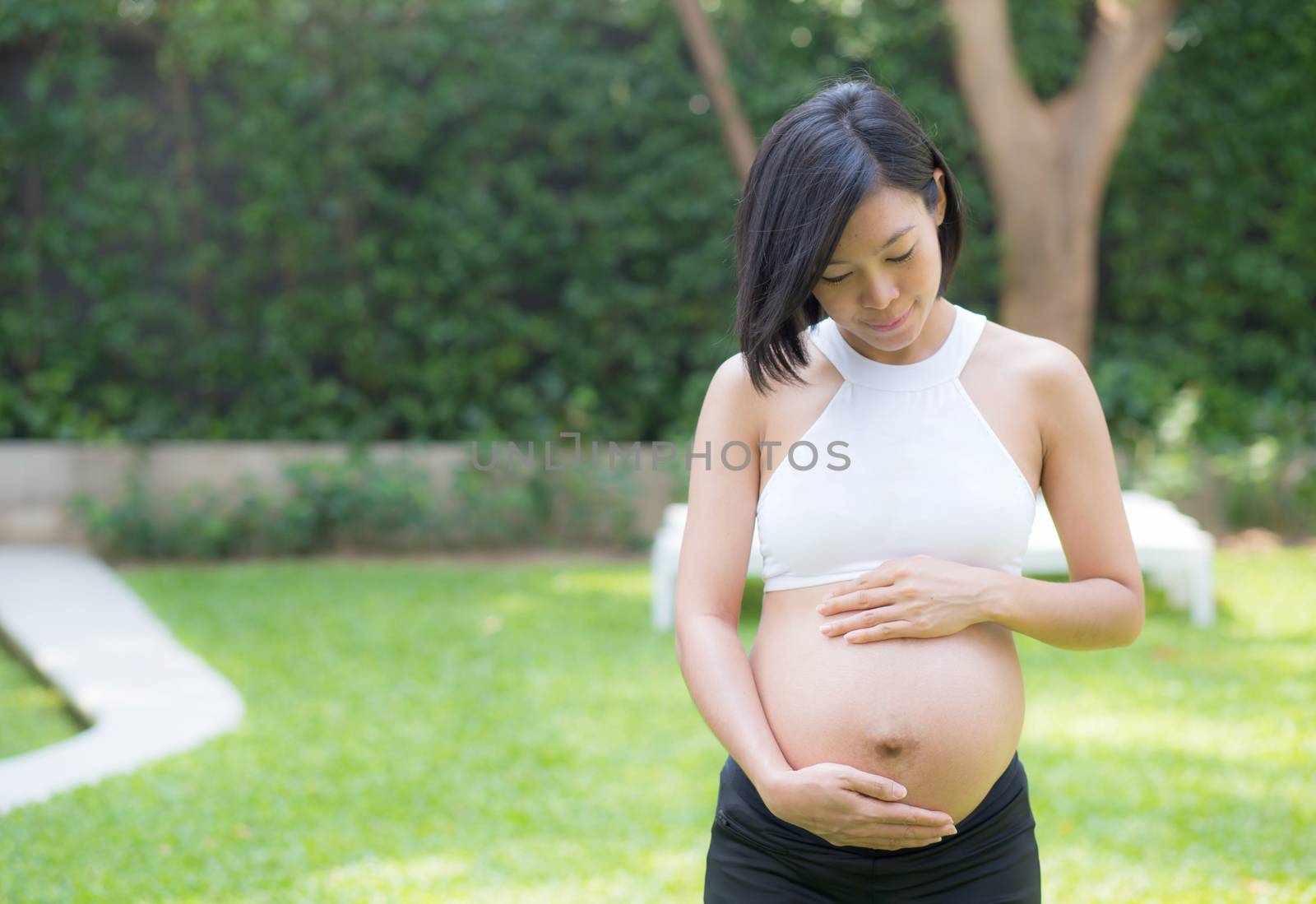 Beautiful pregnant of portrait asian young woman relax in the park, girl with belly standing on grass and yoga exercise for wellness, copy space.