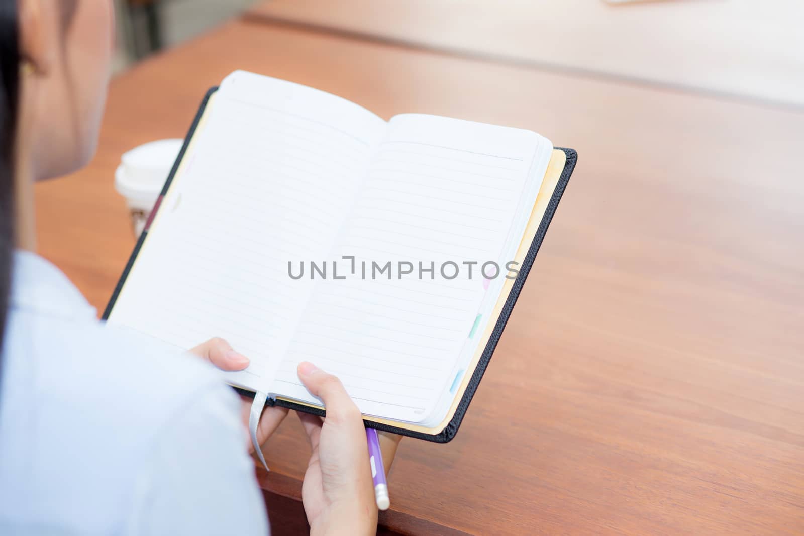 closeup woman hand writing on notebook on wooden table, girl work with paper at coffee shop, top view; freelance business concept.