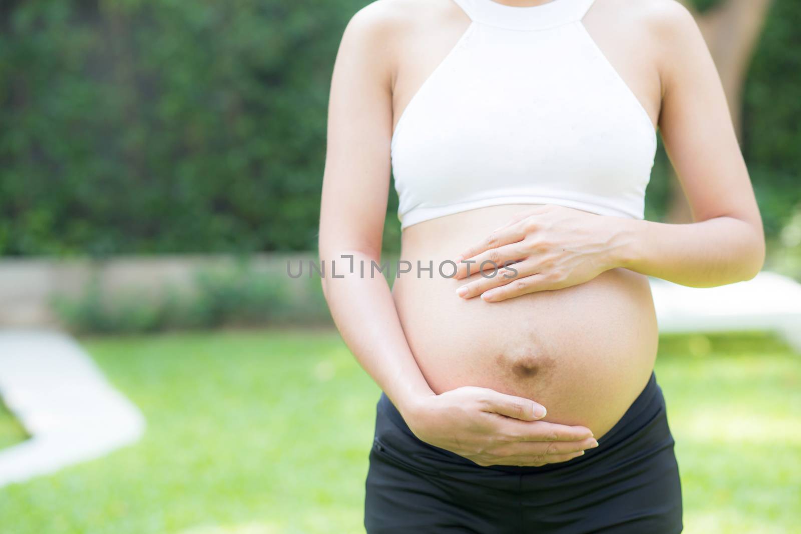 Beautiful pregnant of portrait asian young woman relax in the park, girl with belly standing on grass and yoga exercise for wellness, copy space.