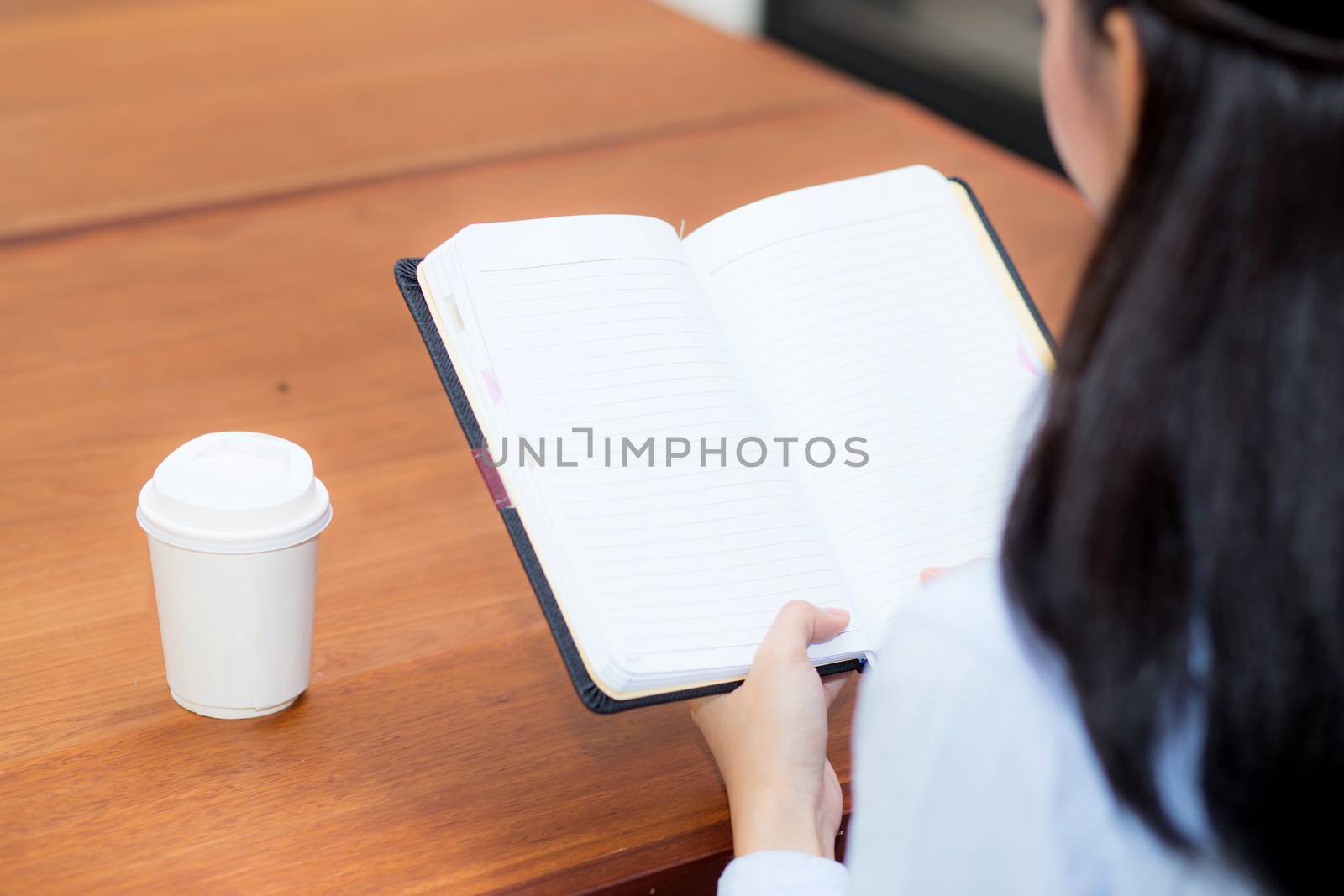 closeup woman hand writing on notebook on wooden table, girl work with paper at coffee shop, top view; freelance business concept.