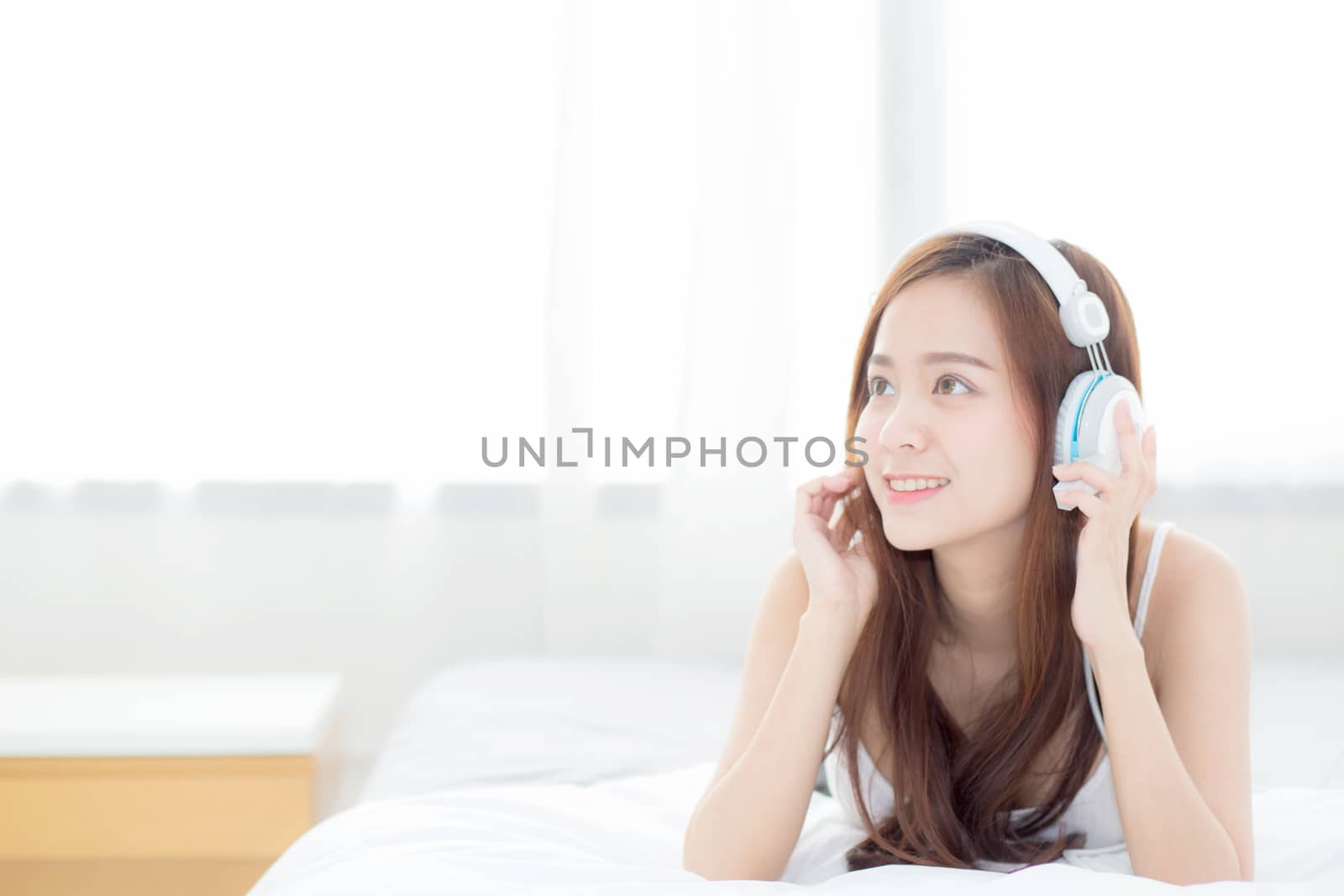 Beautiful asian young woman enjoy listen music with headphone while lying in bedroom, relax girl with earphone internet online, leisure and technology concept.