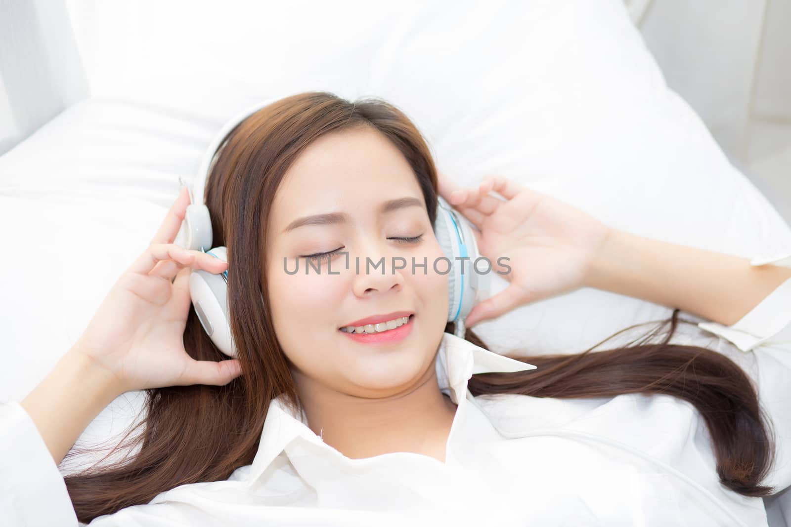 Beautiful asian young woman enjoy listen music with headphone while lying in bedroom, relax girl with earphone internet online, leisure and technology concept.