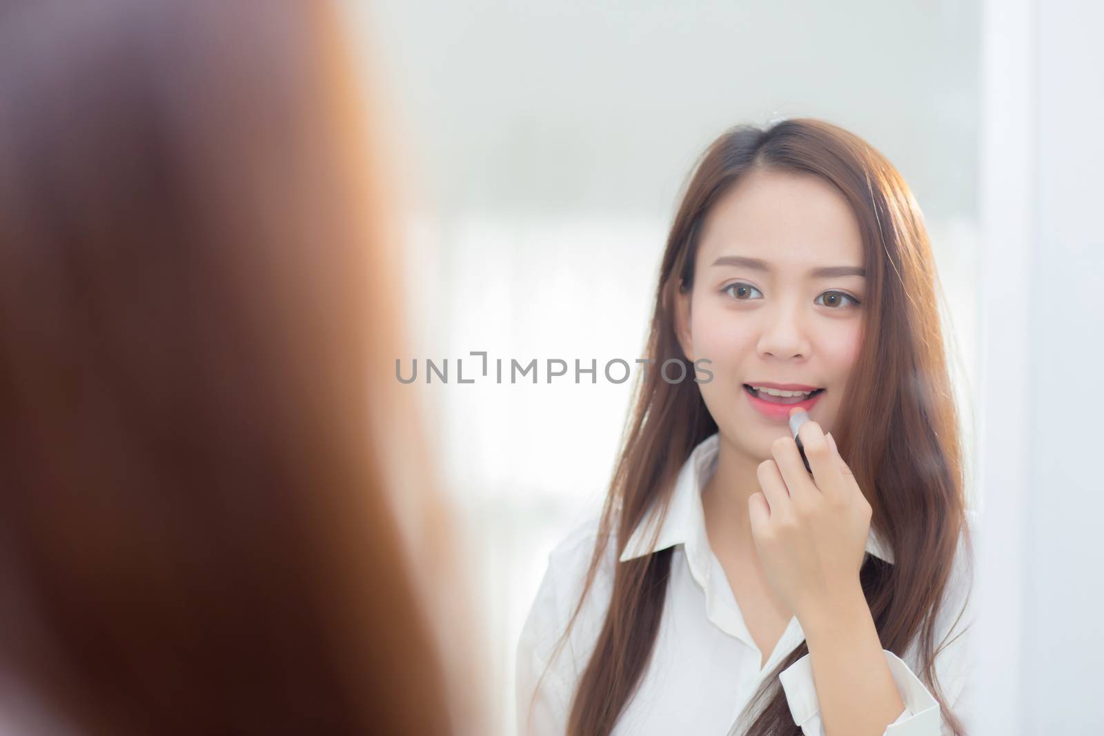 Beauty of portrait of young asian woman at the mirror holding and looking a makeup lipstick, Beautiful girl beauty fashion at the room, lifestyle concept.