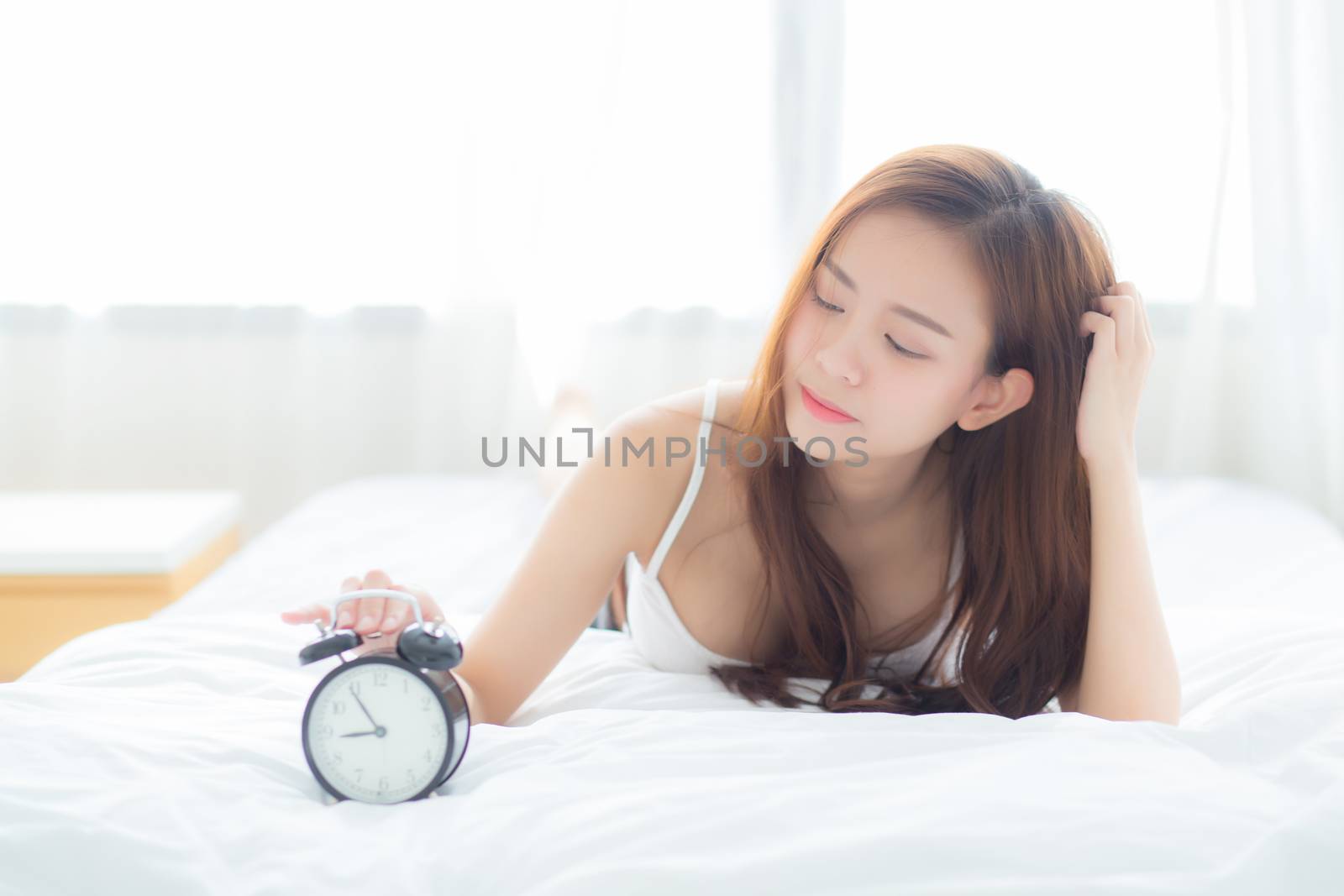 Beautiful asian young woman turn off alarm clock in morning, wake up for sleep with alarm clock, relax and lifestyle concept.