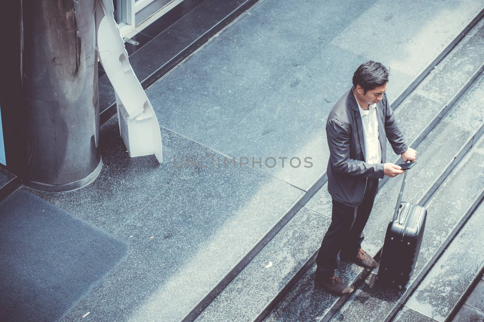 Asian elegant businessman wear suit talking mobile phone while walking holding suitcase outdoor on street, young man contact with customer appointment, communication business concept.