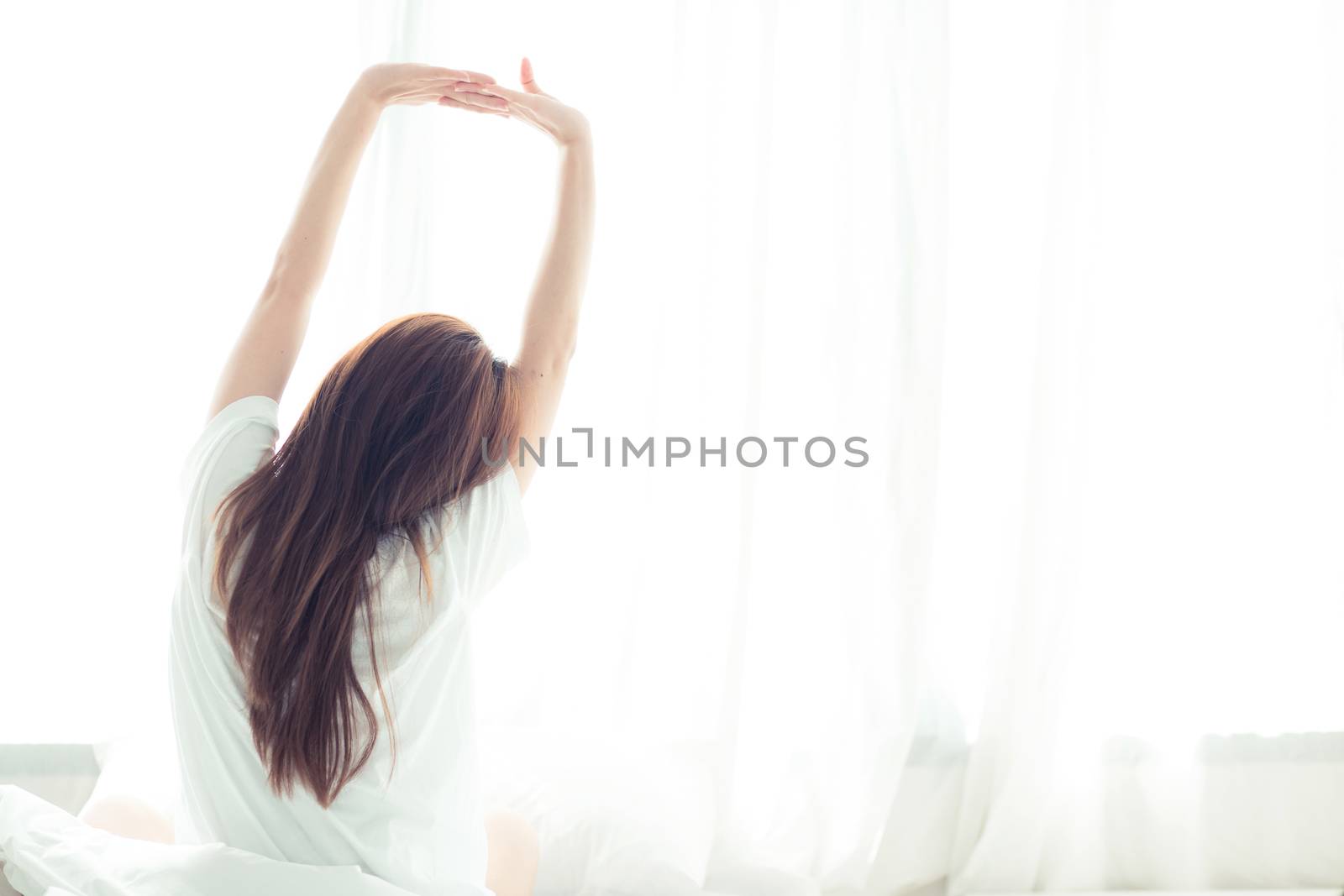 Beautiful young asian woman stretch and relax in bed after wake up morning at bedroom, back view, new day and resting for wellness, lifestyle concept.
