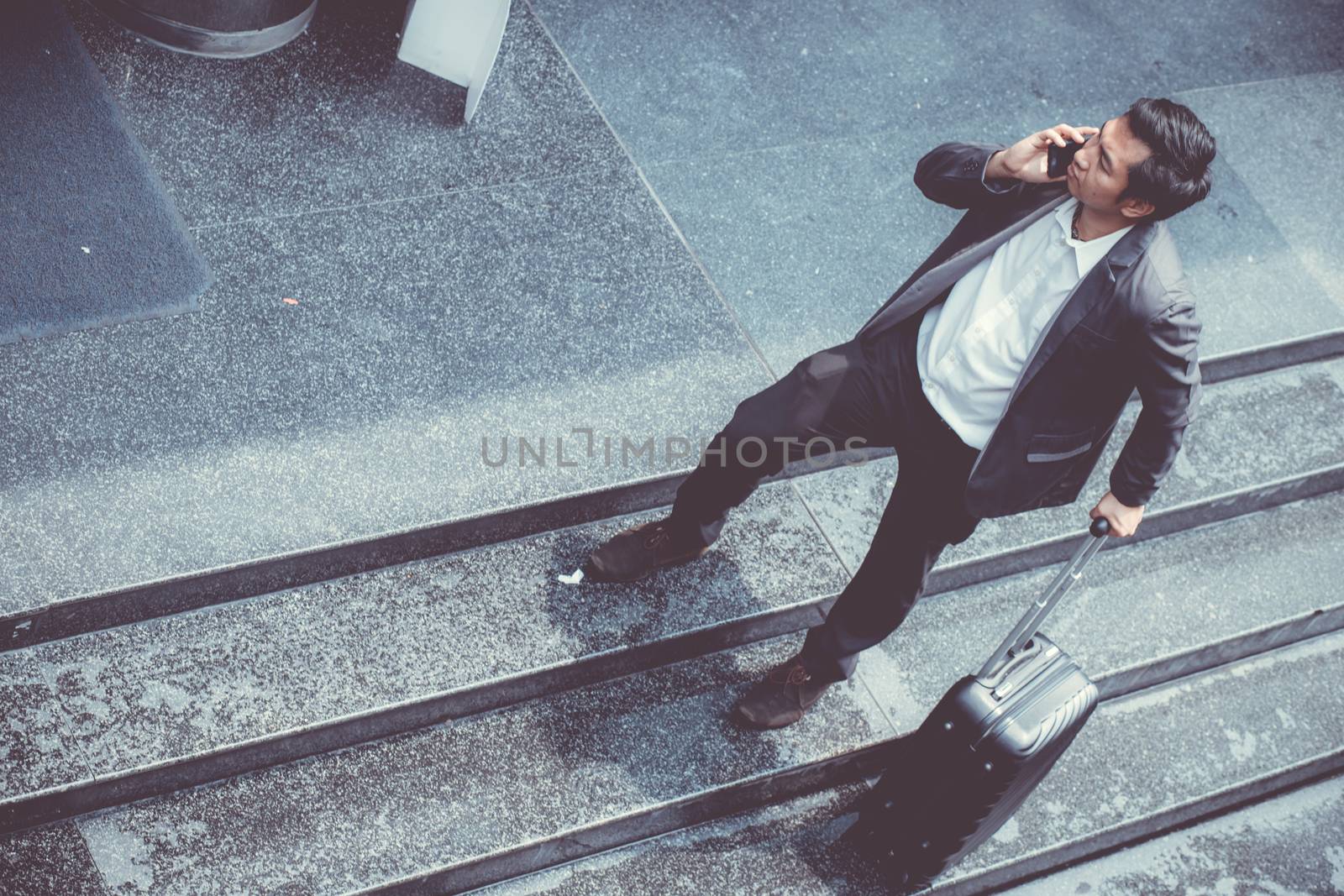 Asian elegant businessman wear suit talking mobile phone while walking holding suitcase outdoor on street, young man contact with customer appointment, communication business concept.