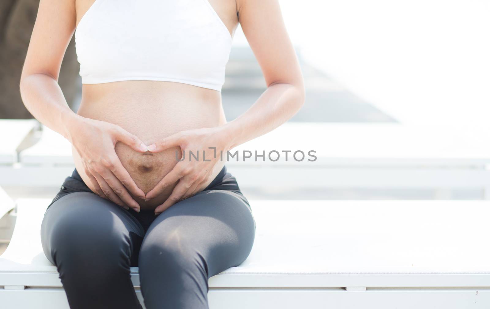 closeup beautiful pregnant asian young woman relax in the park, girl with belly sitting at swimming pool for wellness, copy space.