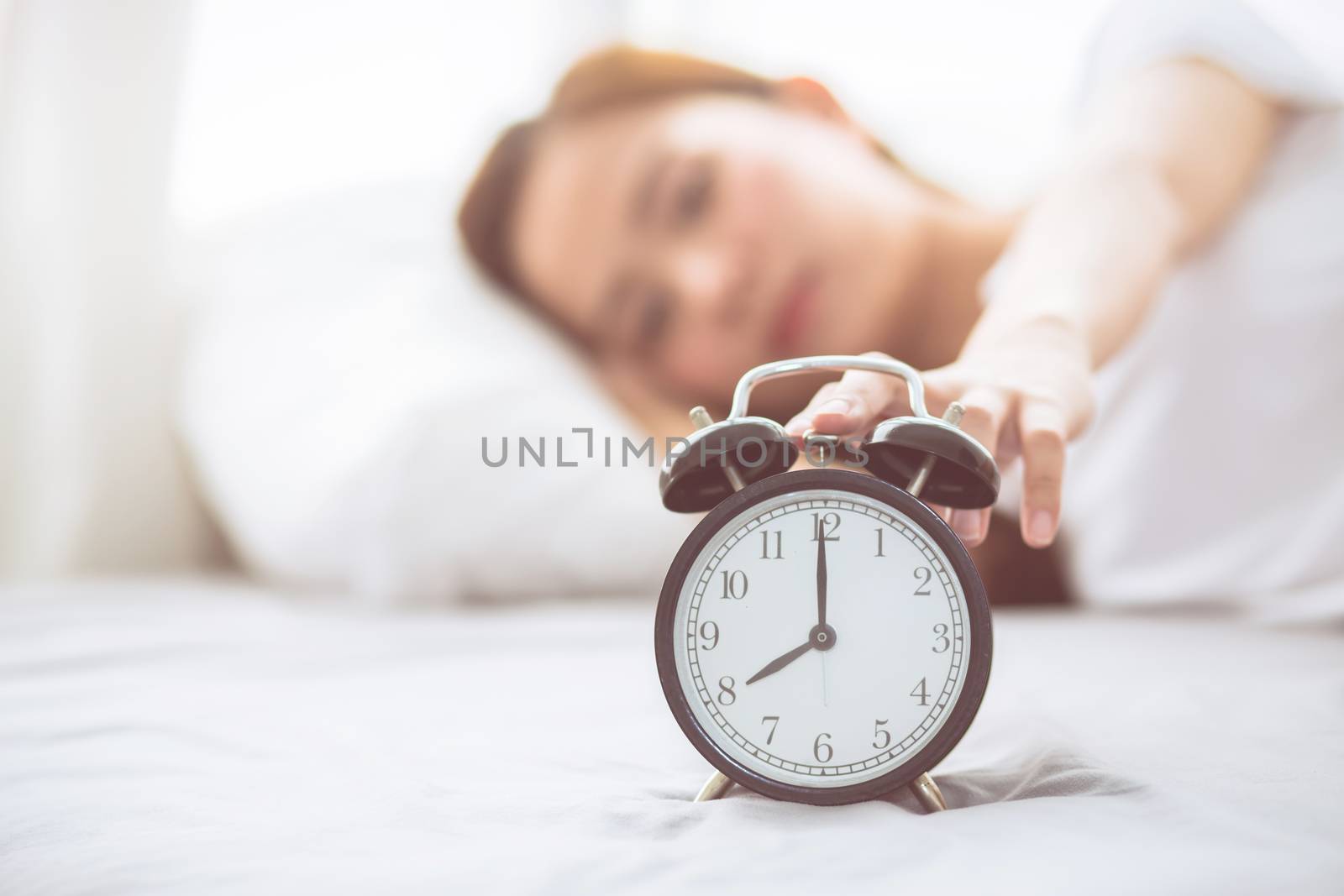 Beautiful asian young woman turn off alarm clock in good morning, wake up for sleep with closeup foreground alarm clock, relax and lifestyle concept.