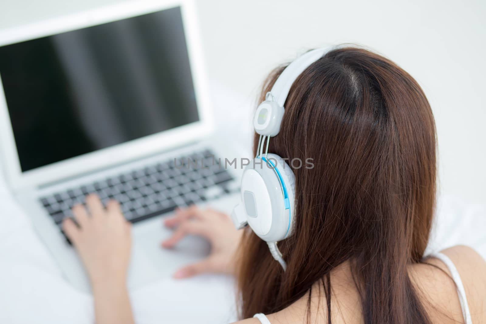 Beautiful asian young woman relax listening to music with headphone and laptop online internet on vacation in bedroom, cheerful of asia girl leisure, top view, lifestyle concept.