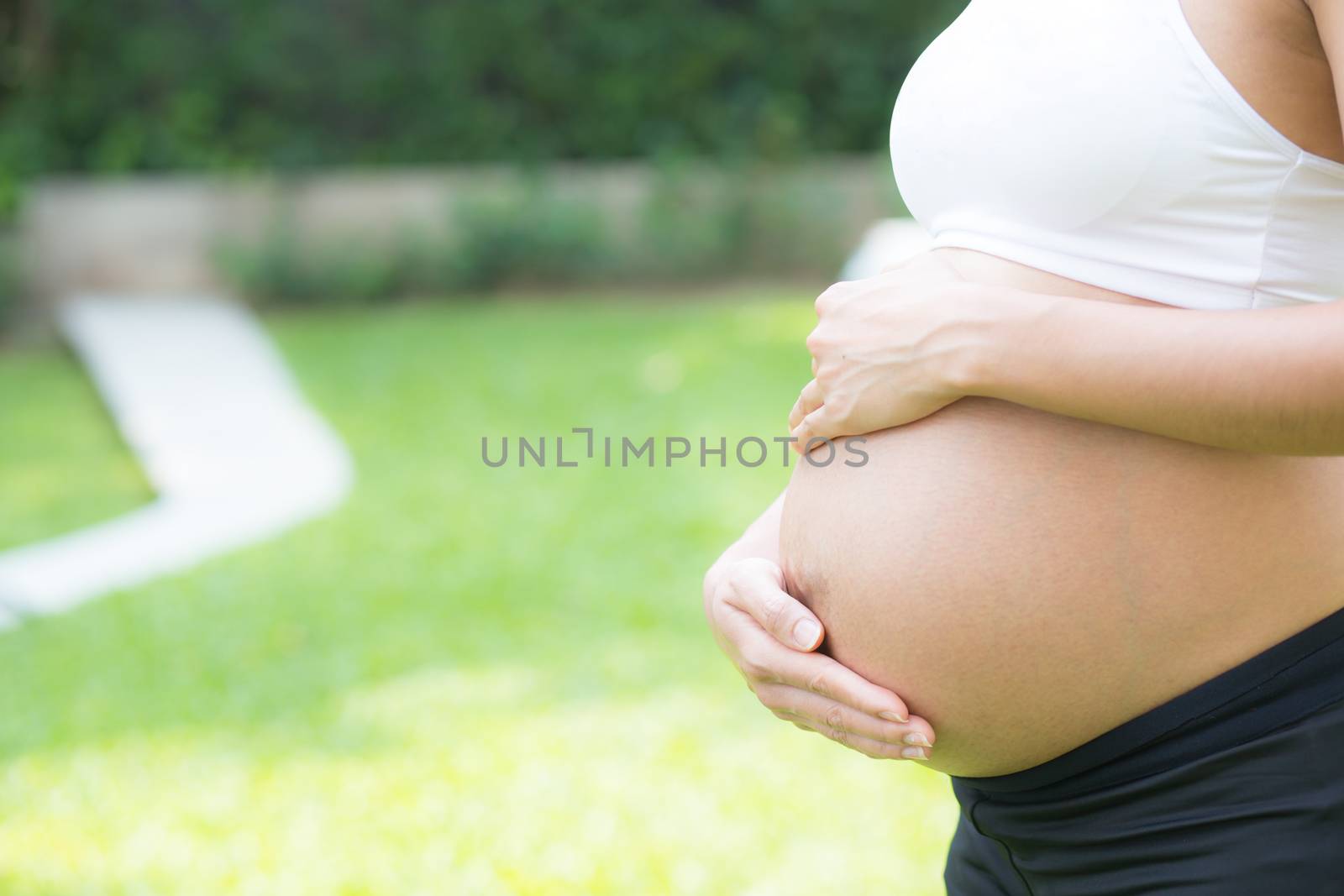 Beautiful pregnant asian young woman relax in the park, girl with belly standing on grass and yoga exercise for wellness, copy space.
