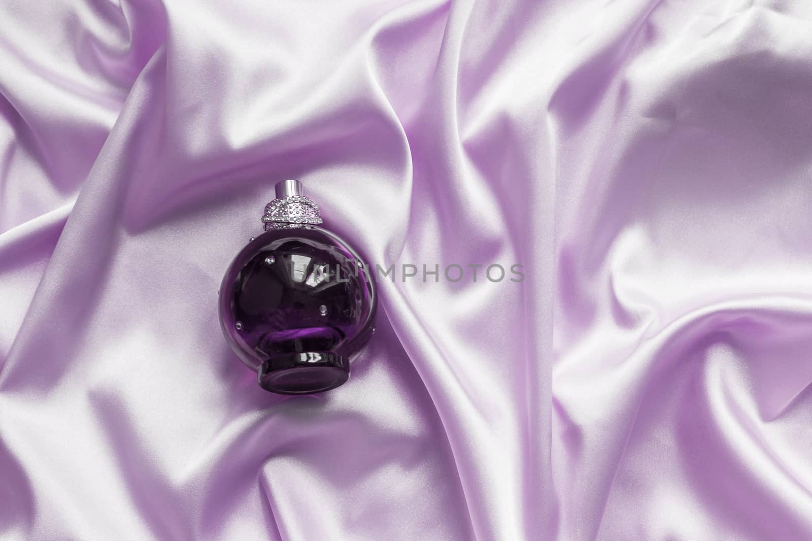 Perfume bottle on lilac silk folded fabric background. Luxery Scent fragrance cosmetic beauty product.