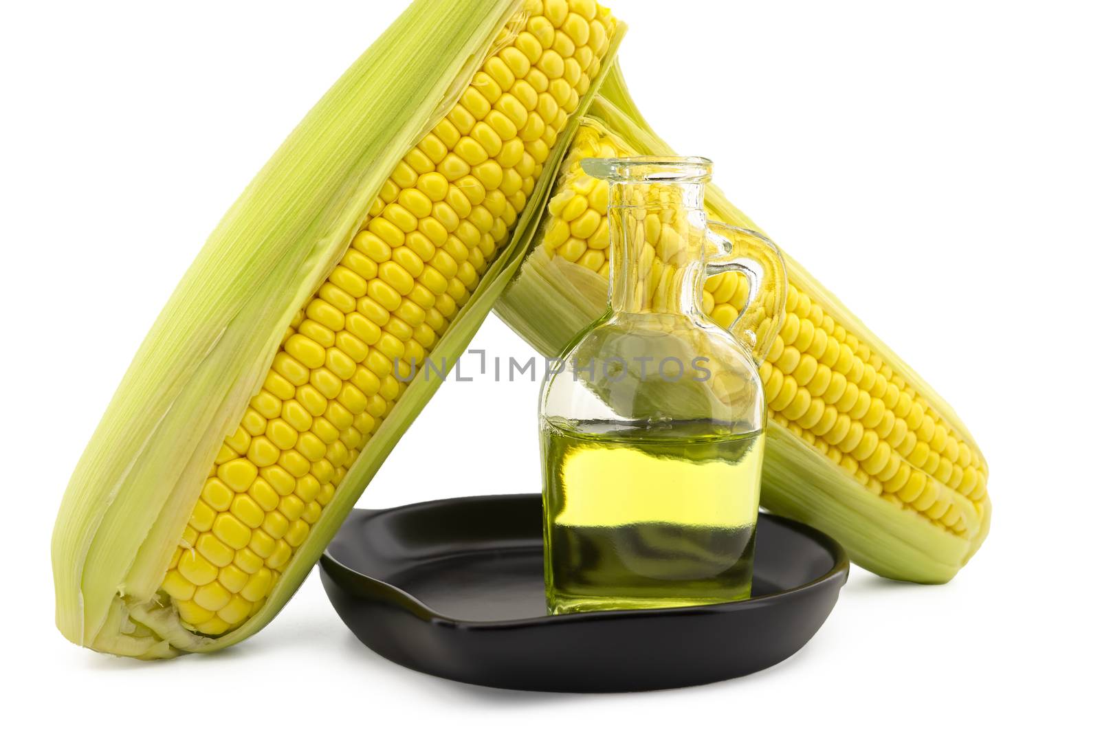 Corn oil in decanter in the cast iron skillet and fresh corncobs next to the cast iron skillet isolated on white background with free copy space for text