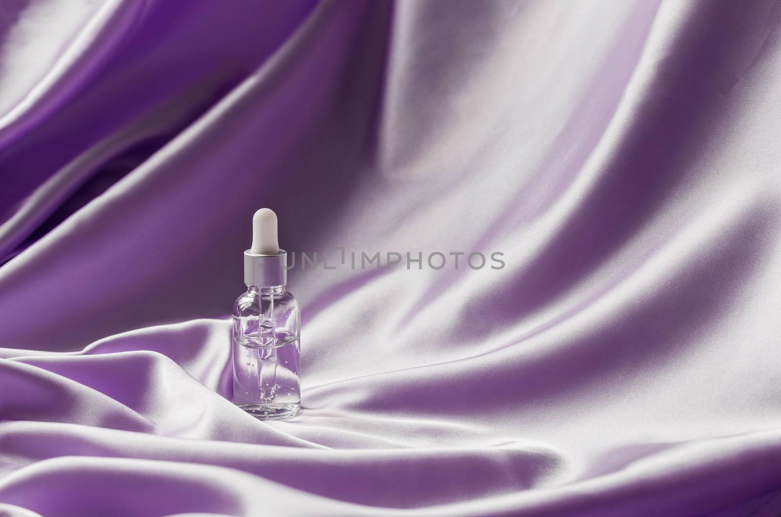Face serum on lilac silk folded fabric background. Luxery cosmetic beauty product.
