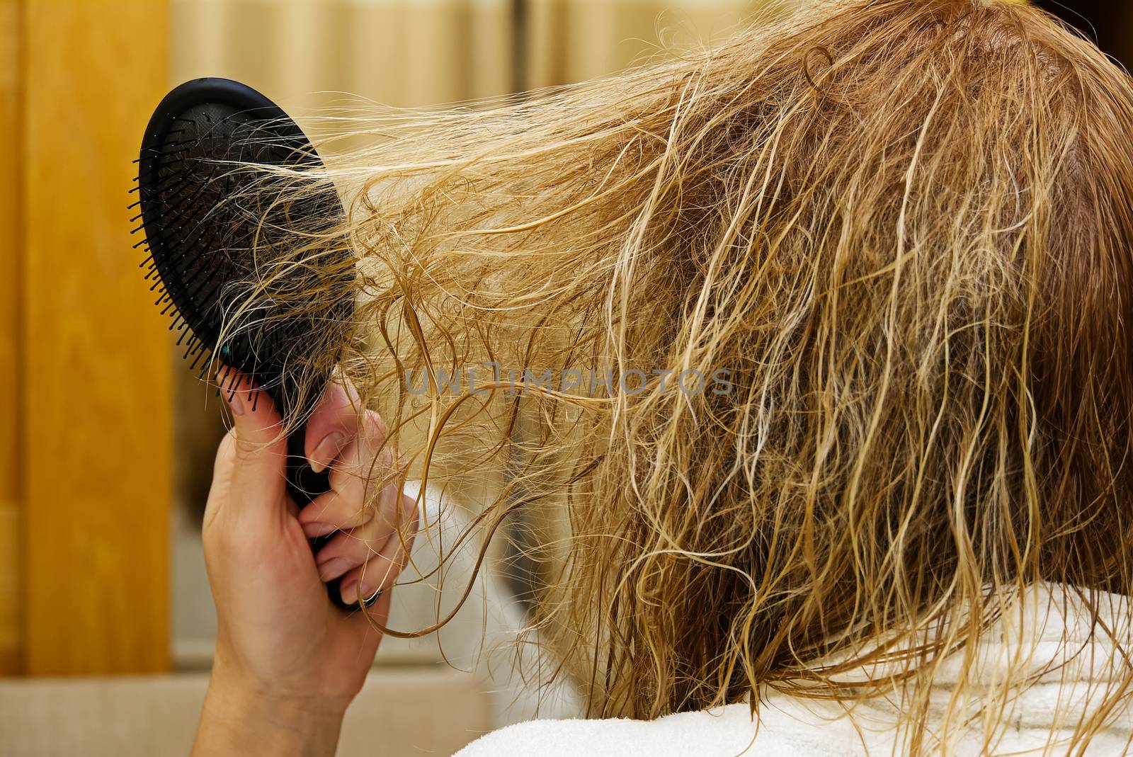 blond combing wet and tangled hair. Young woman combing her tangled hair after shower in hotel interior, close-up.